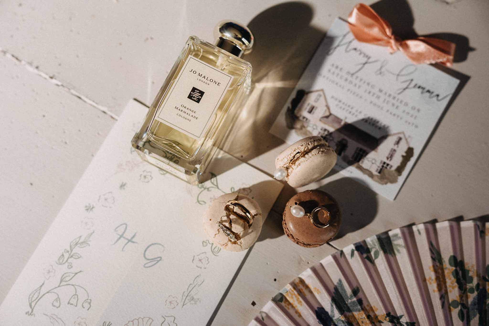Jo Malone cologne with gold-leaf macarons, venue illustration invitation, sage floral card, and mauve paper fan