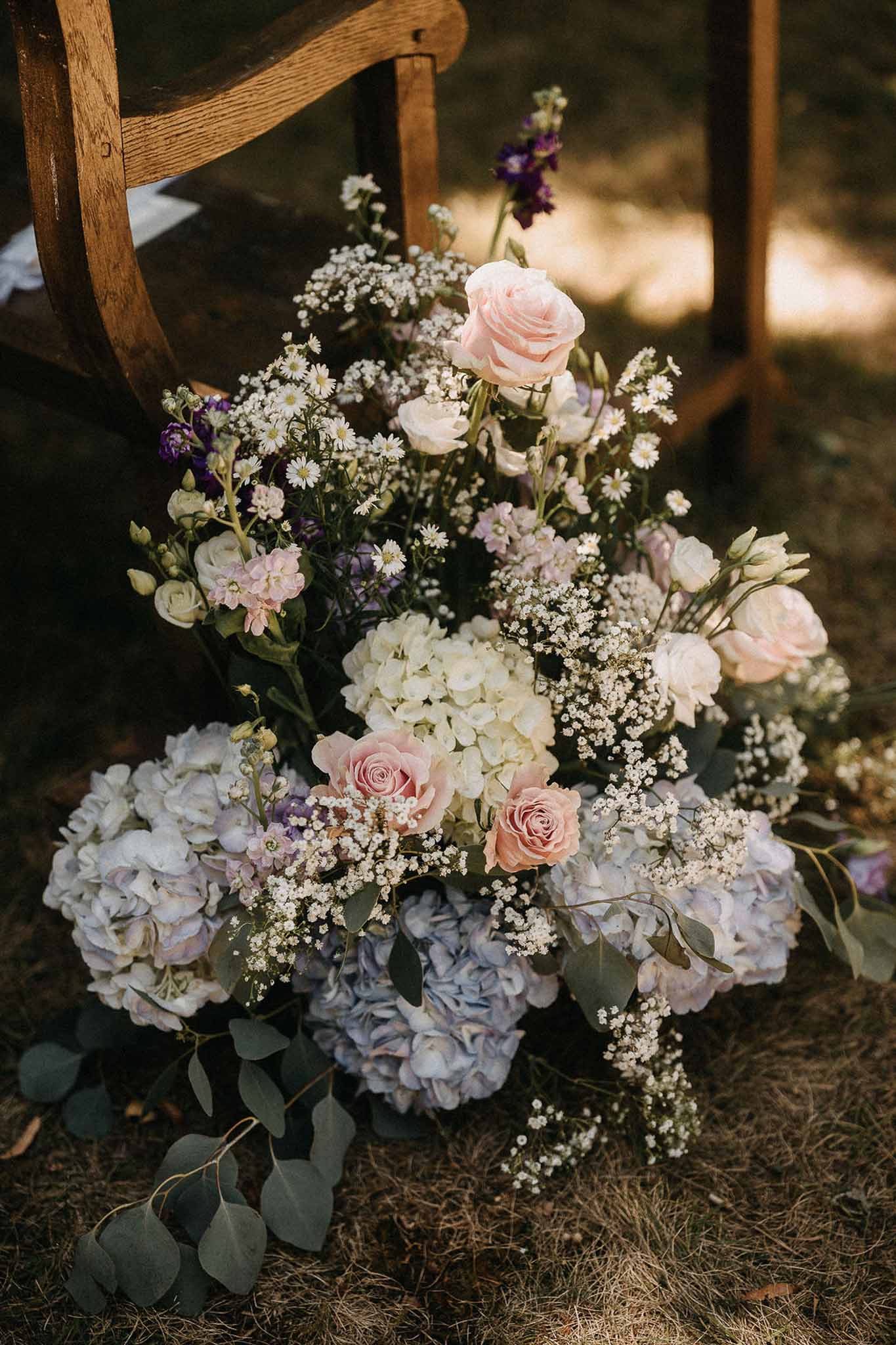 Ceremony aisle arrangement of blue hydrangeas blush roses purple stock and trailing eucalyptus