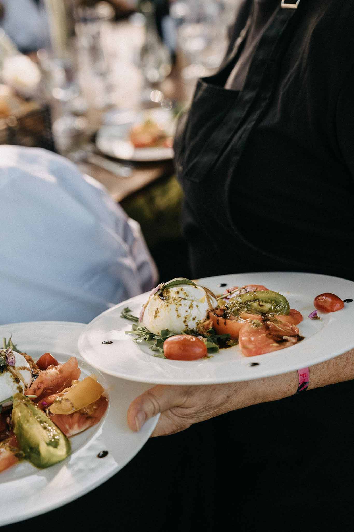 Server carrying burrata and heirloom tomato salad plates during wedding reception dinner service