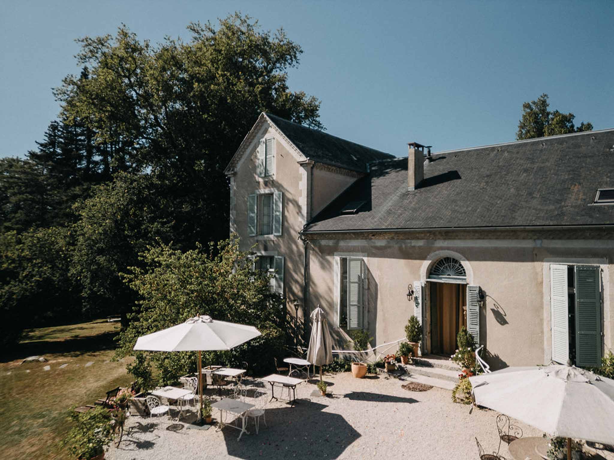 Elevated view of pale stone French manor house with grey-blue shutters and terrace set with bistro tables