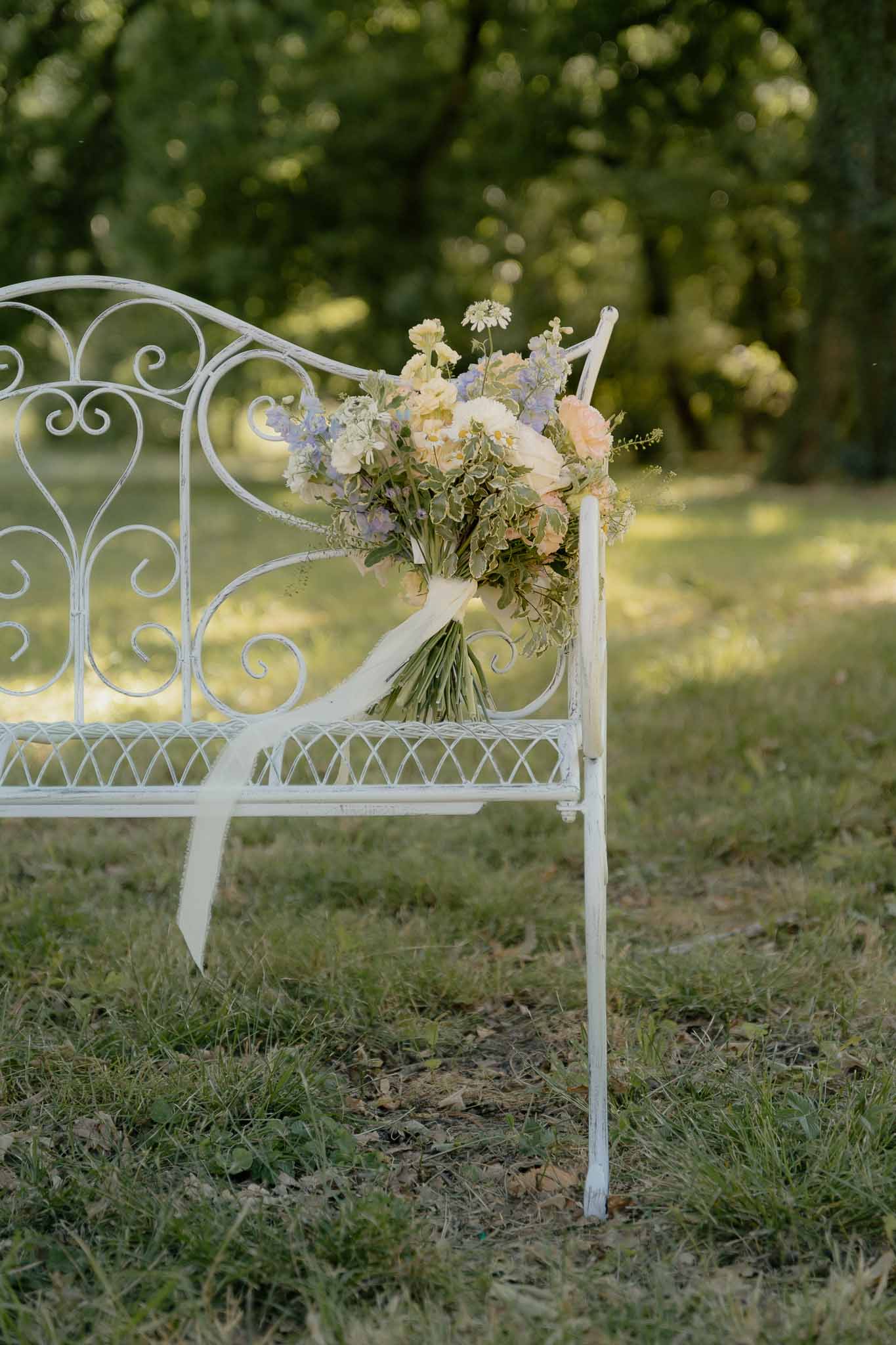 Bridal bouquet of peach roses, lavender delphinium, and ivory ranunculus with satin ribbon on iron bench