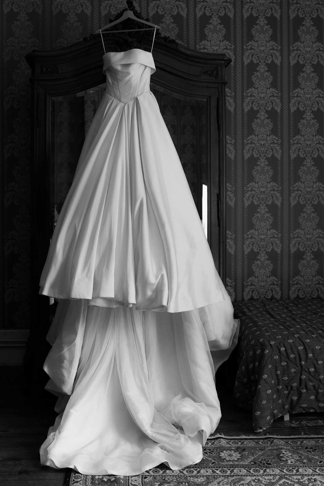 Black and white strapless ballgown with tiered skirt hanging from wooden armoire in damask room
