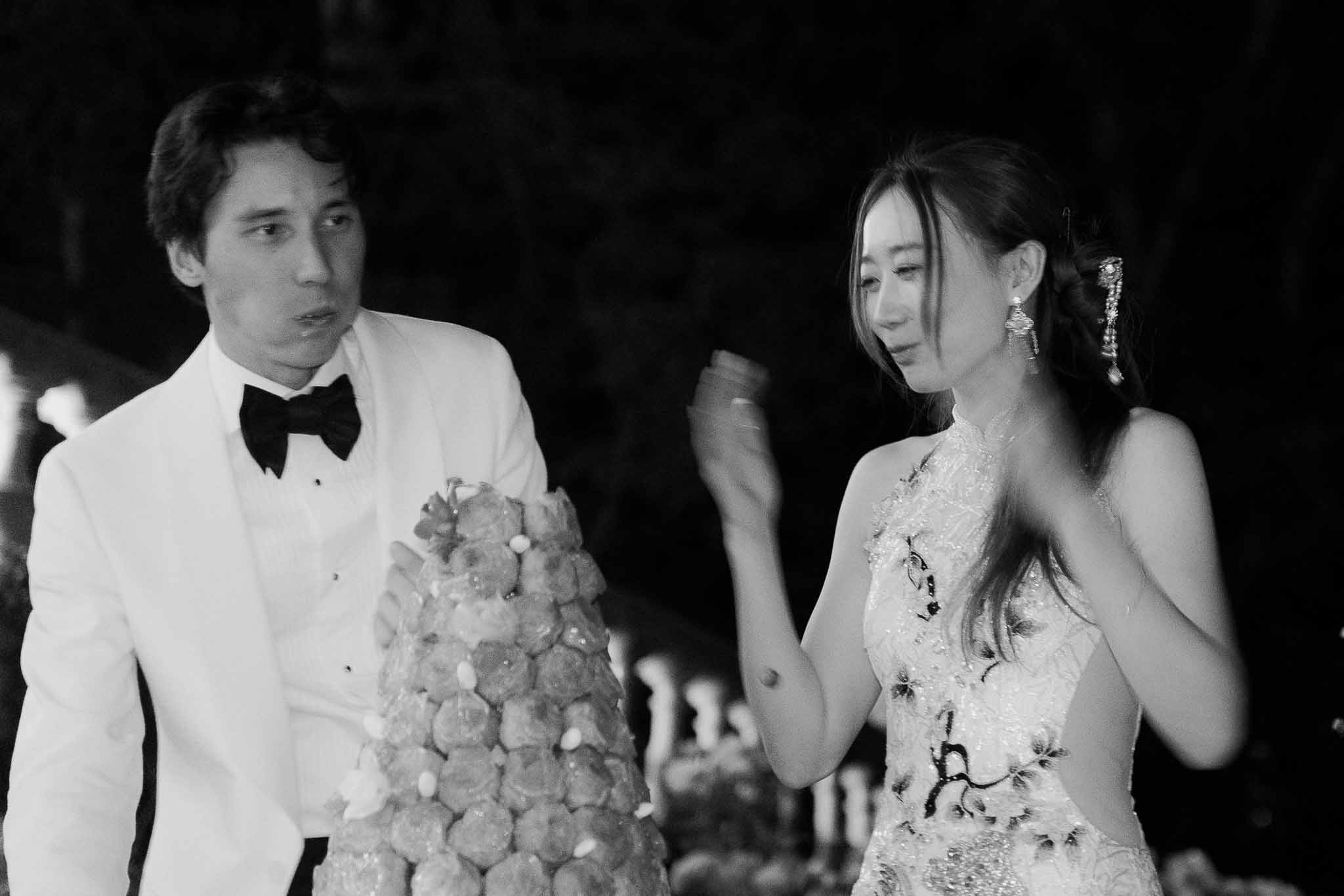 Black and white couple laughing beside croquembouche tower at evening reception with candles