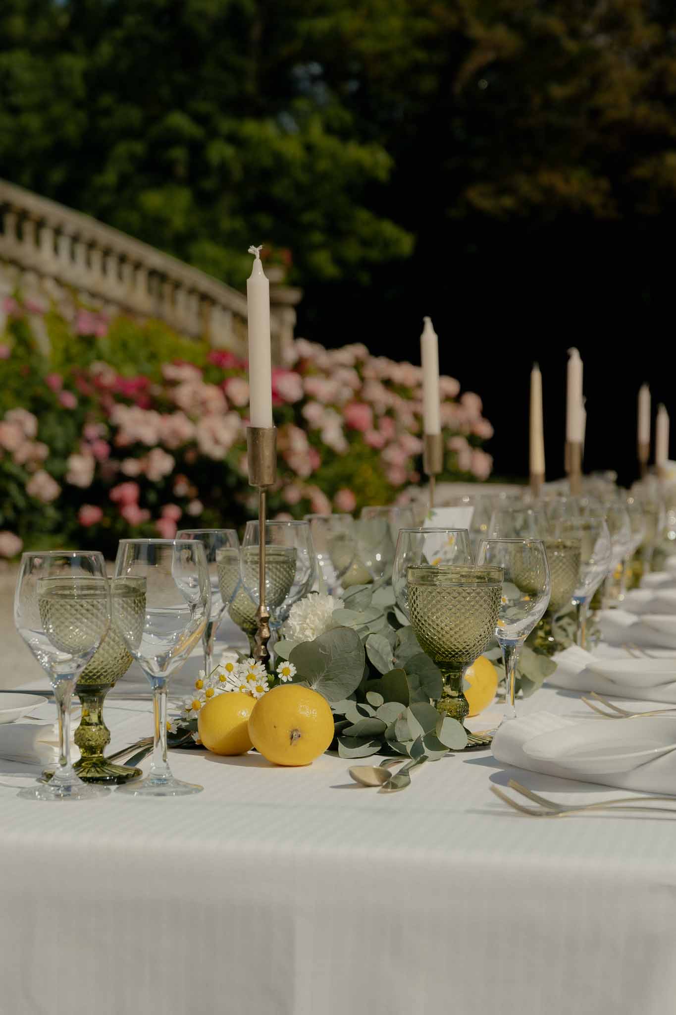 Mediterranean tablescape with lemons, eucalyptus, white daisies, olive hobnail glasses, and brass candlesticks