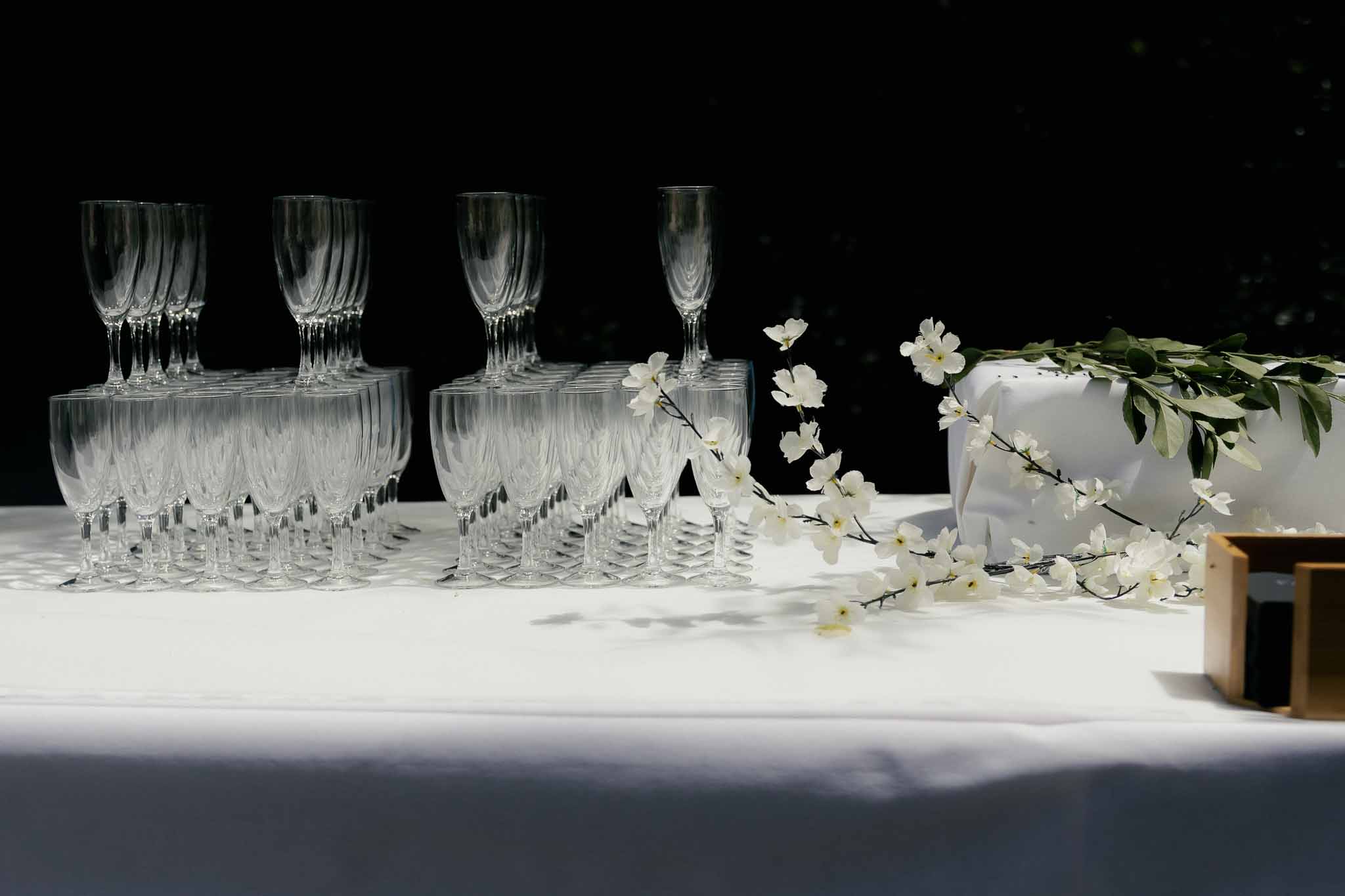 Rows of crystal champagne flutes on white linen table with white blossom branch decoration