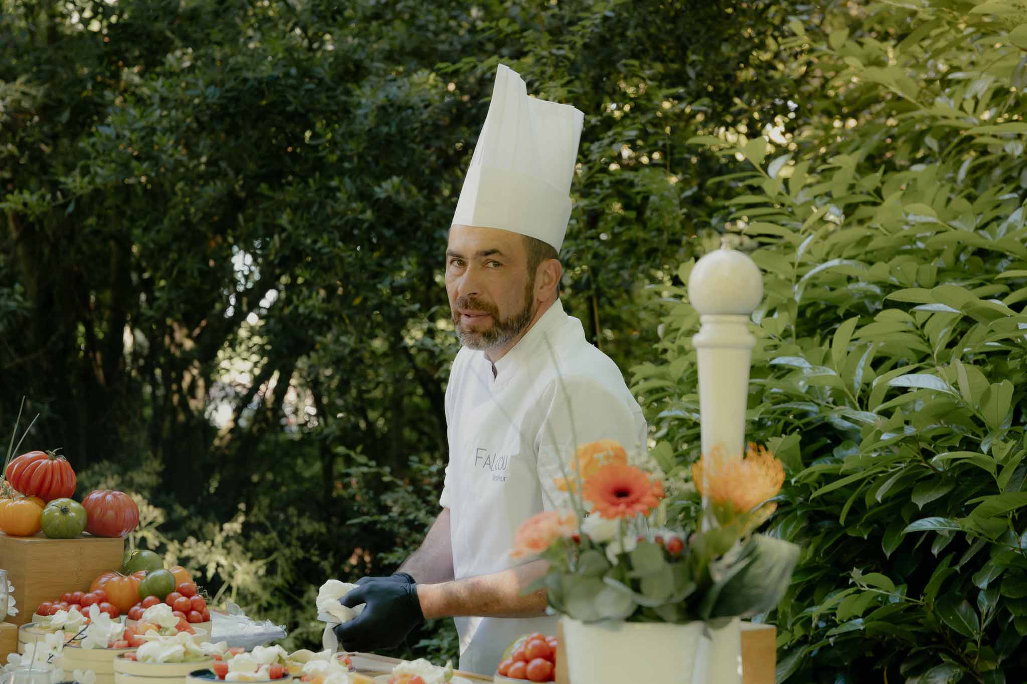 Chef in white jacket preparing heirloom tomato and cheese spread at outdoor catering station