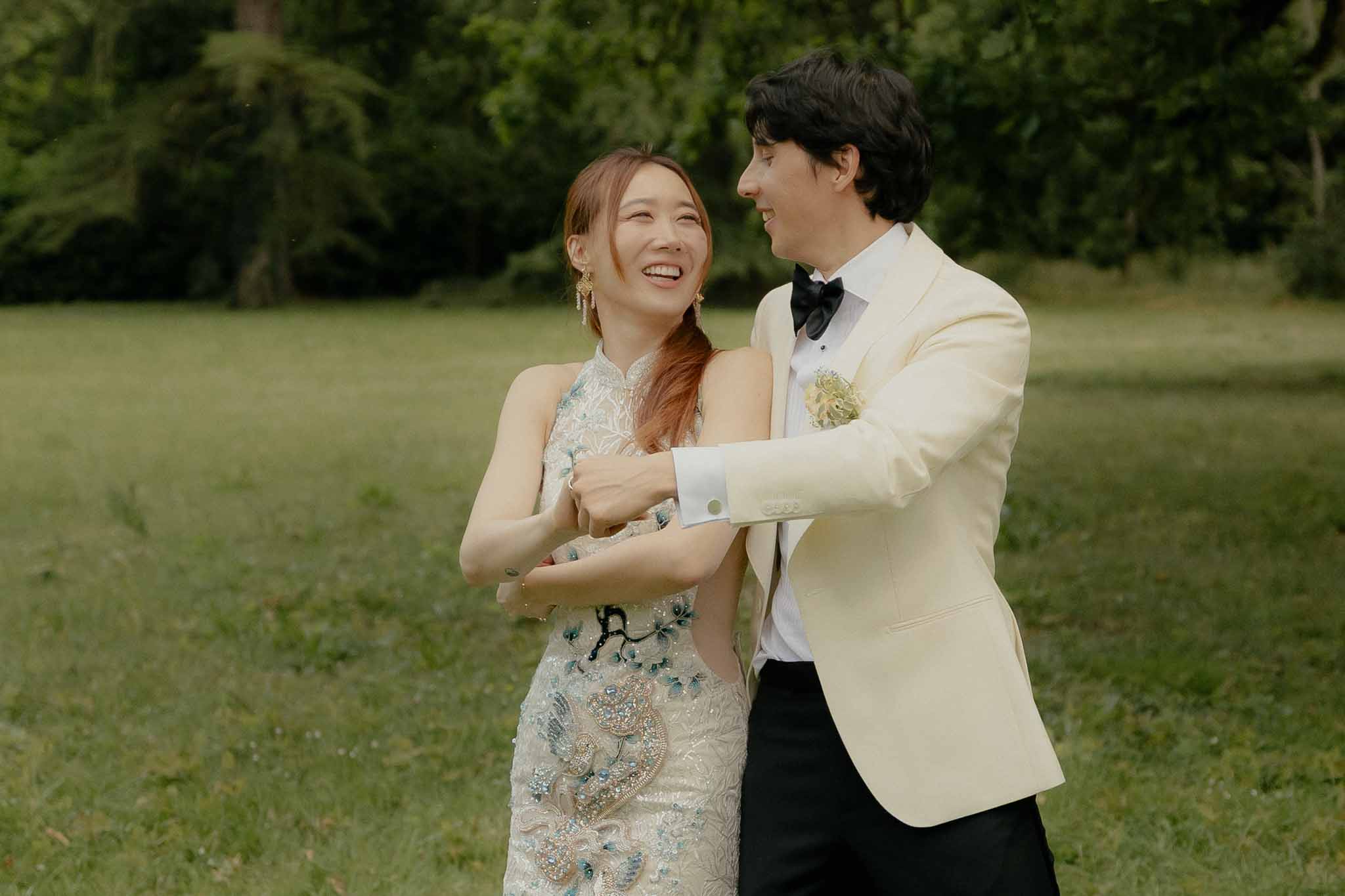 Laughing couple holding hands with bride in ivory qipao-style dress with blue floral embroidery