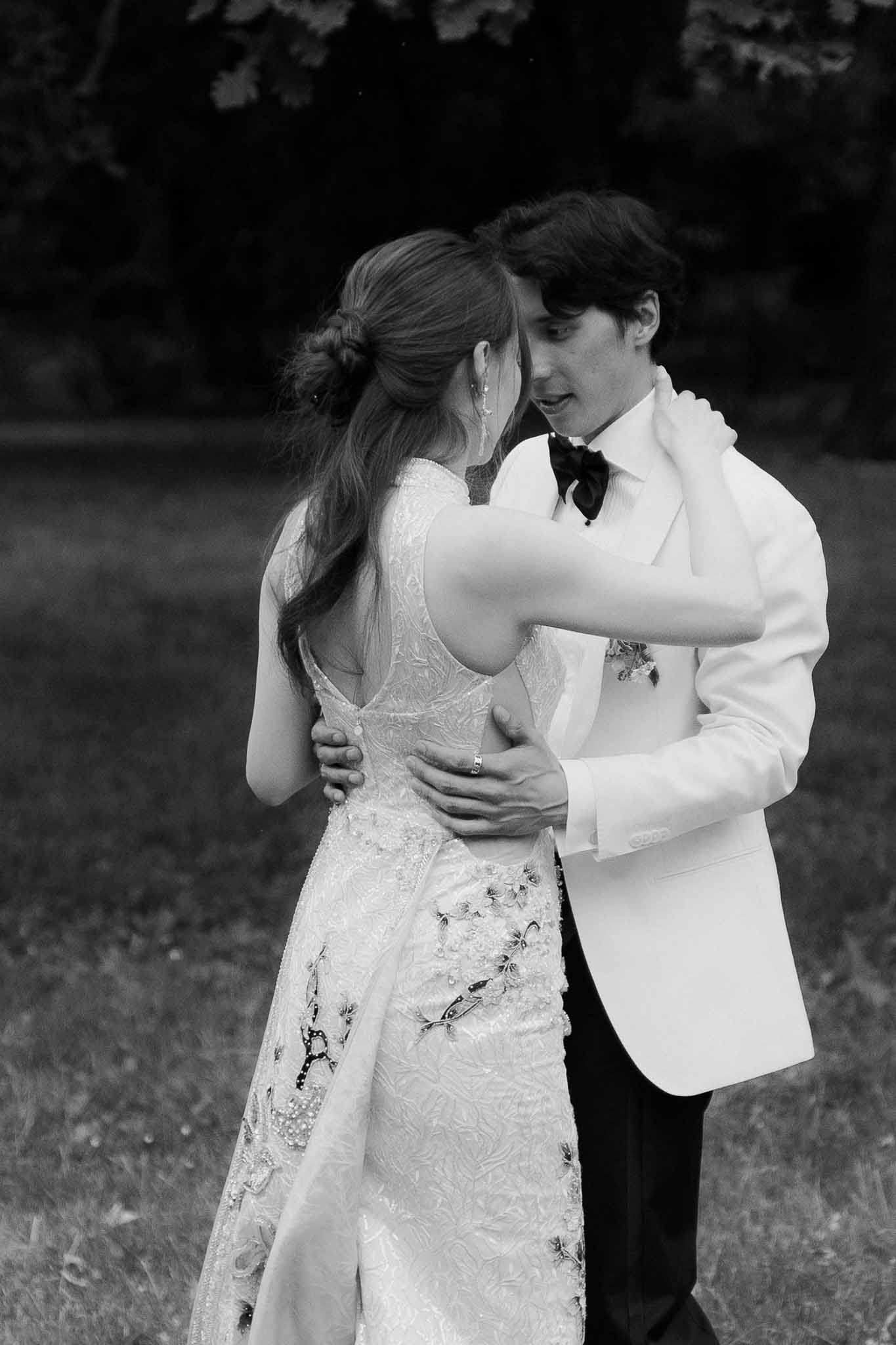 Black and white of couple dancing on lawn, bride in embellished lace gown, groom in white dinner jacket