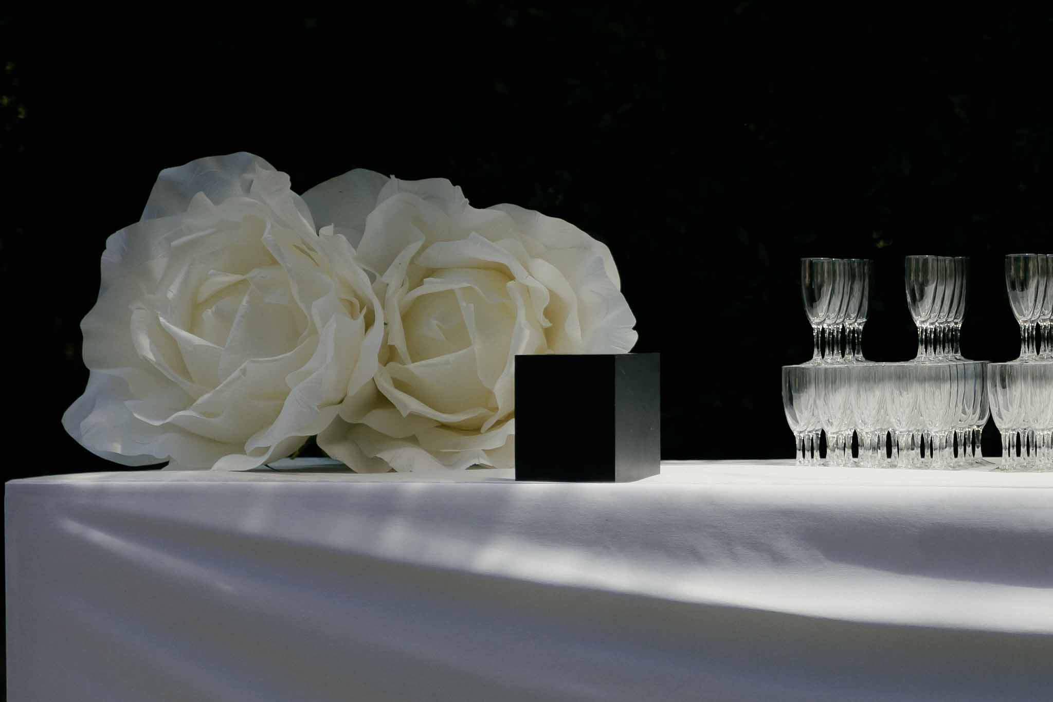 Oversized white paper roses with black cube accent and stacked crystal glasses on white linen
