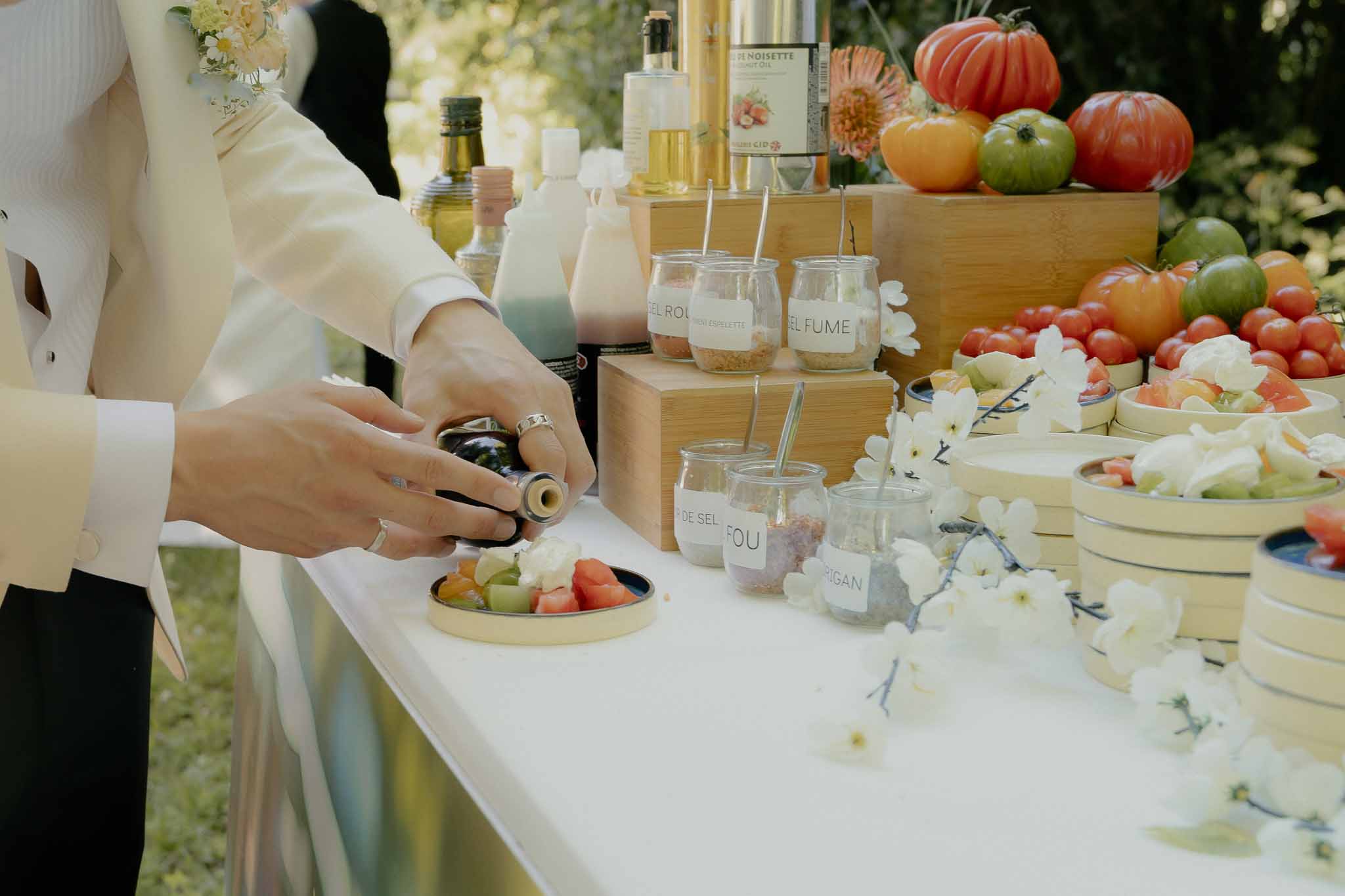 Artisanal tomato bar with labeled salt jars, olive oil bottles, and heirloom tomatoes in wooden crates