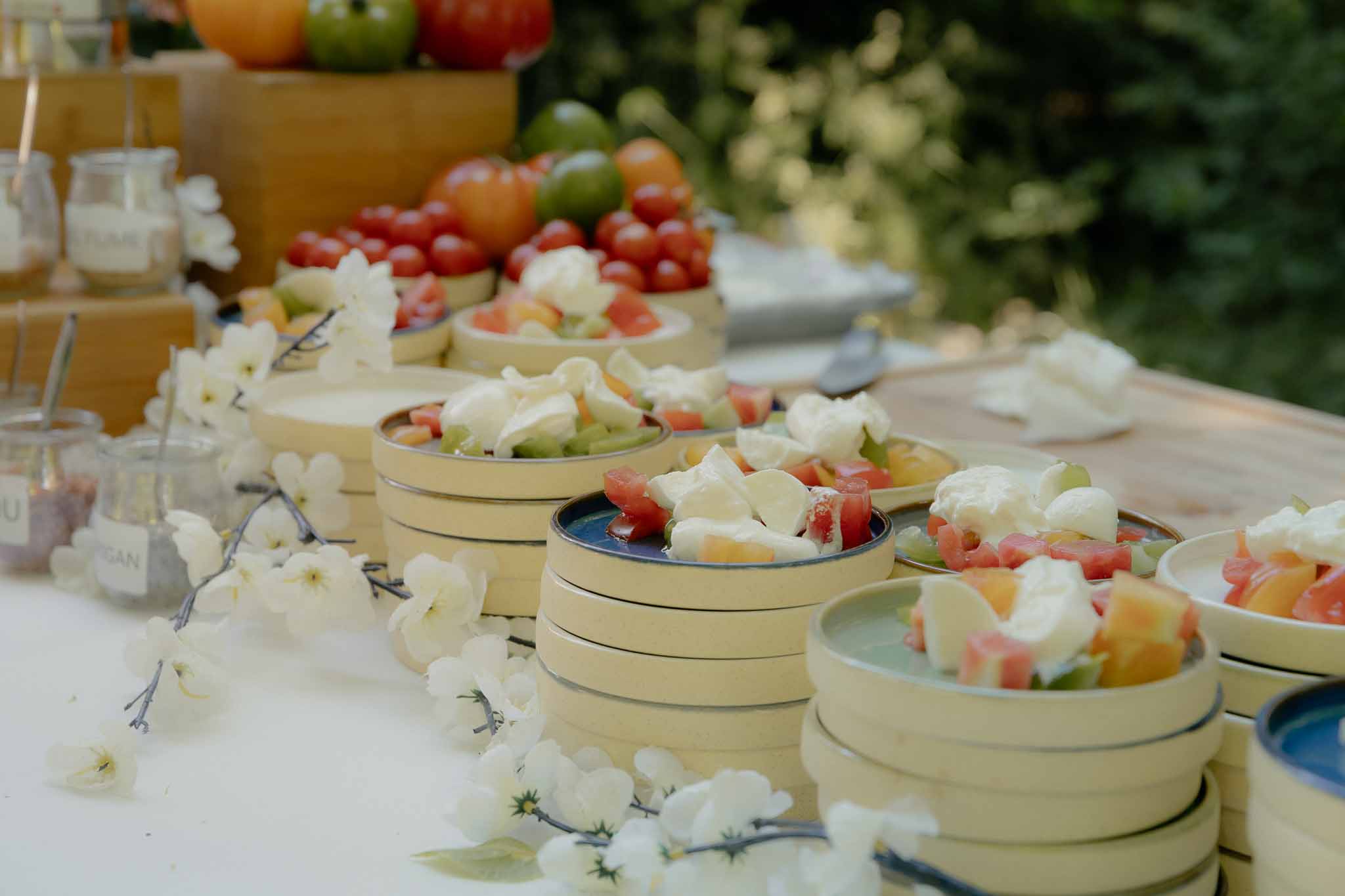 Stacked bowls of watermelon and mozzarella salad with heirloom tomato crate and vegan labels on buffet