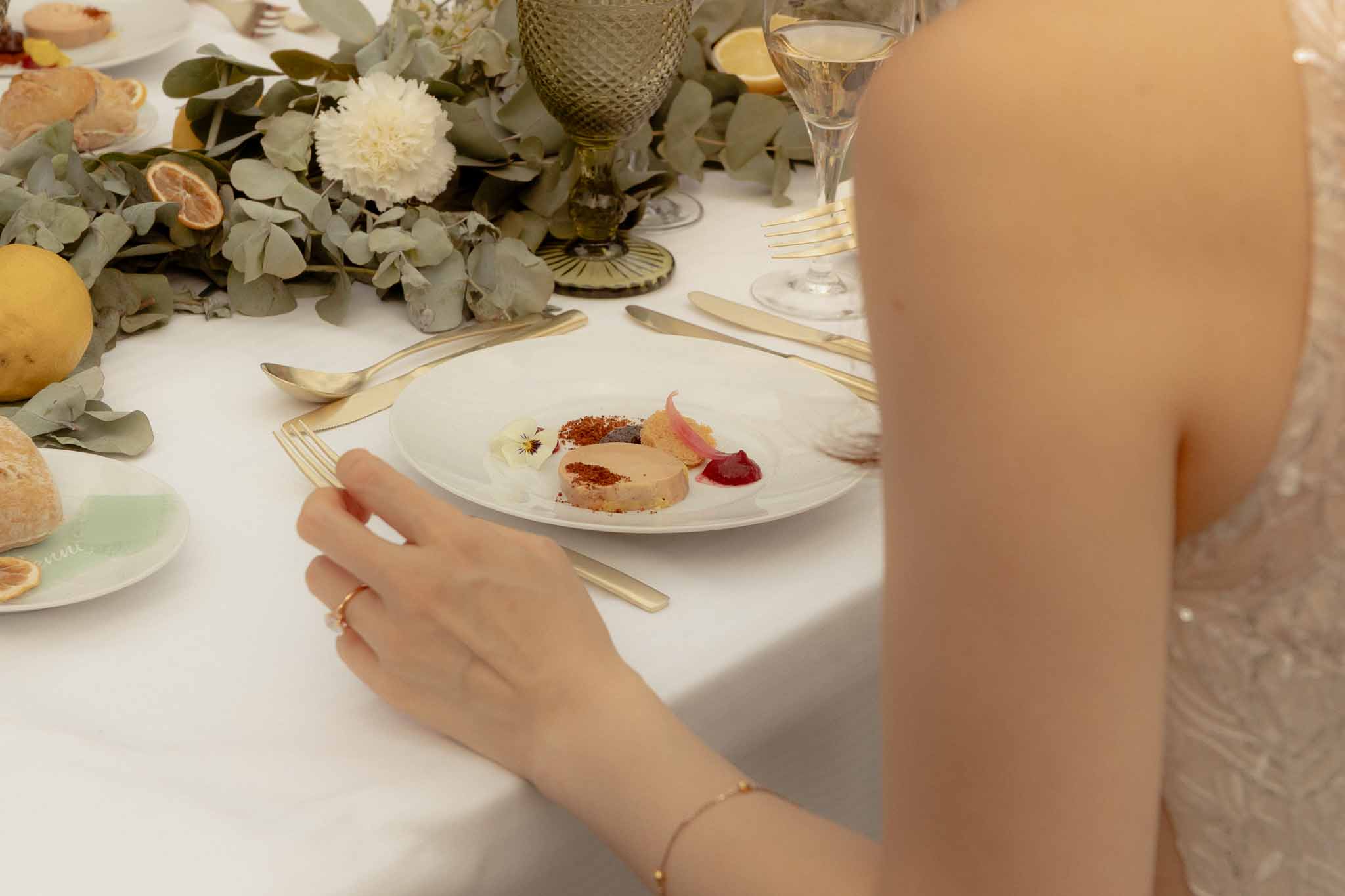 Foie gras starter on white plate with eucalyptus, lemon, and chrysanthemum runner beside sage goblets and gold cutlery