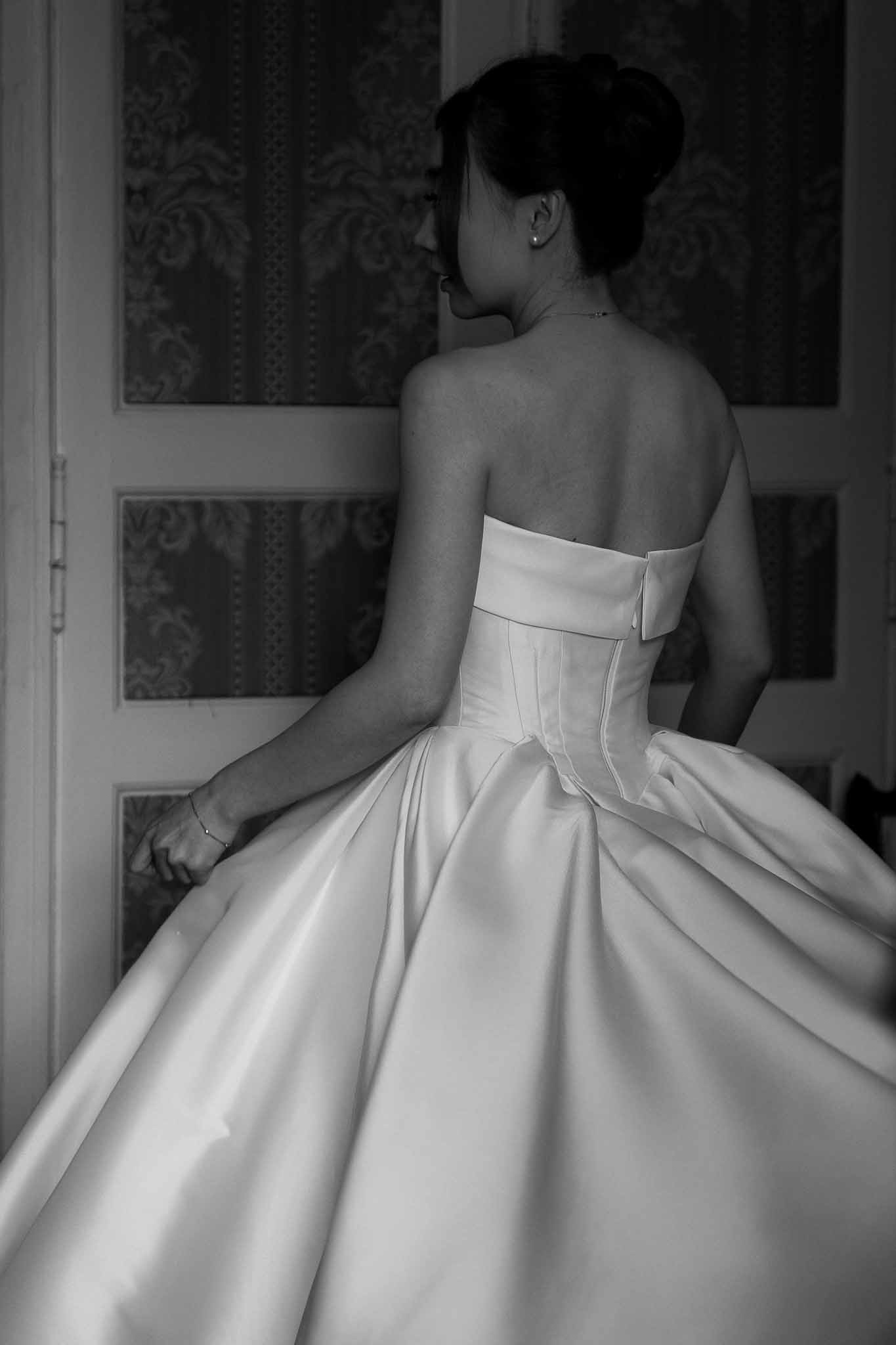 Bride from behind in strapless corset ballgown with bow detail before ornate panelled doors in B&W