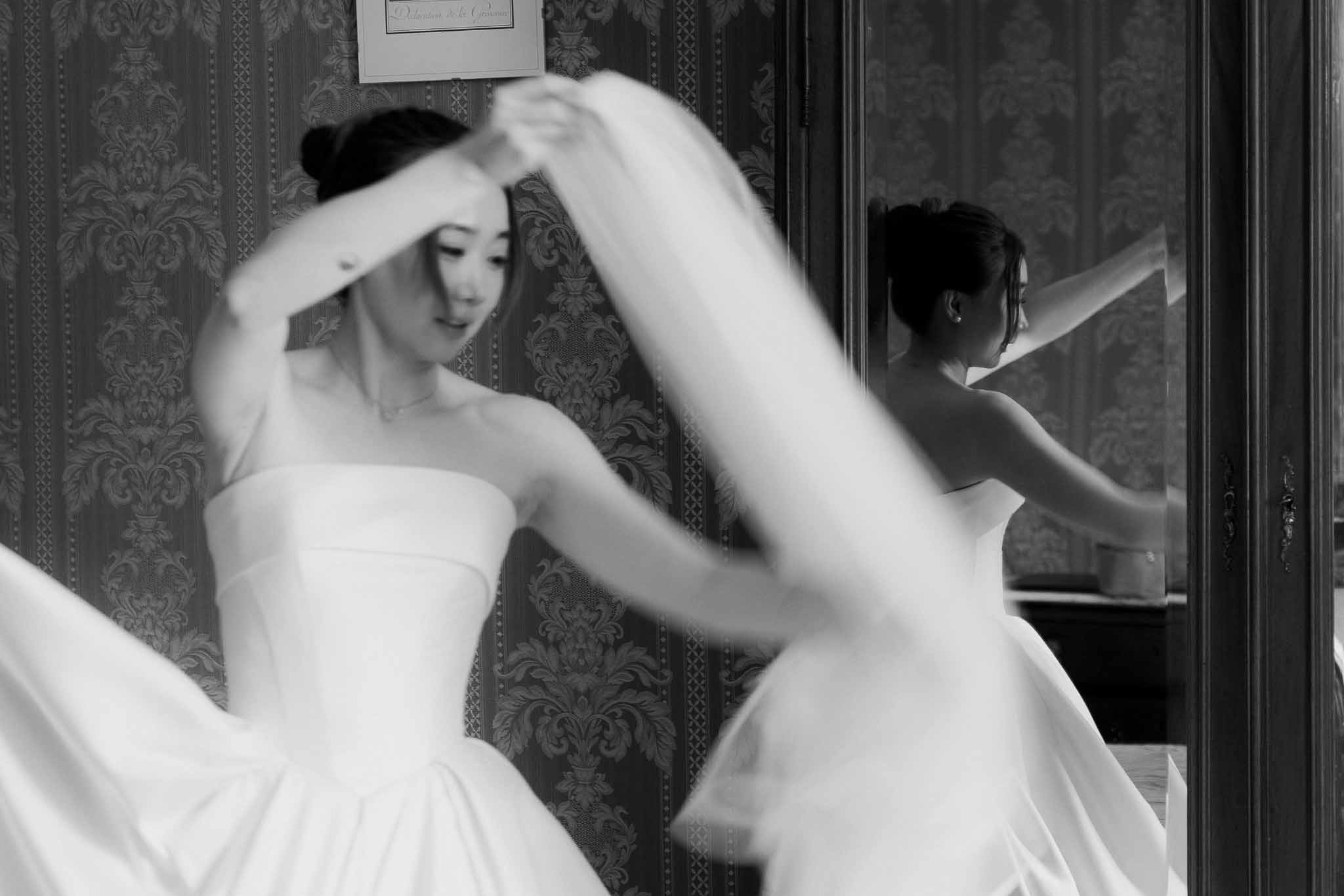Black and white bride adjusting veil in motion blur before damask wallpaper with mirror reflection
