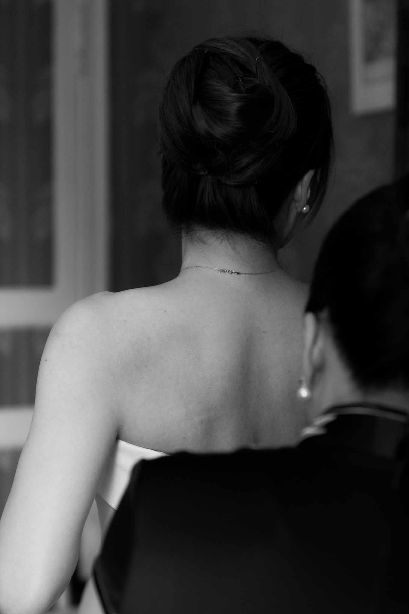 Black and white close-up of bride's French twist updo with pearl earring and back tattoo