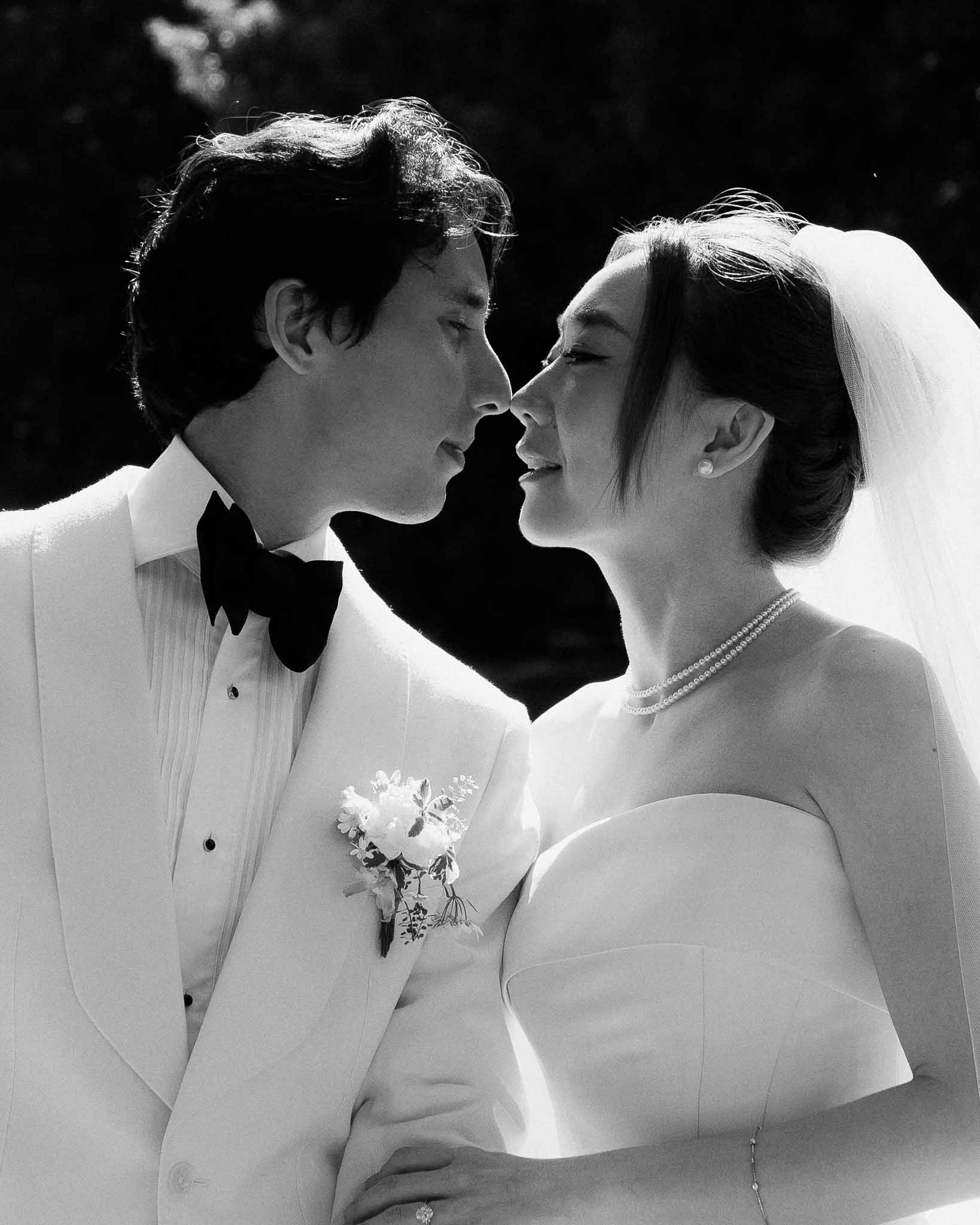 Black and white close-up of couple nose to nose with dramatic directional light on dark background