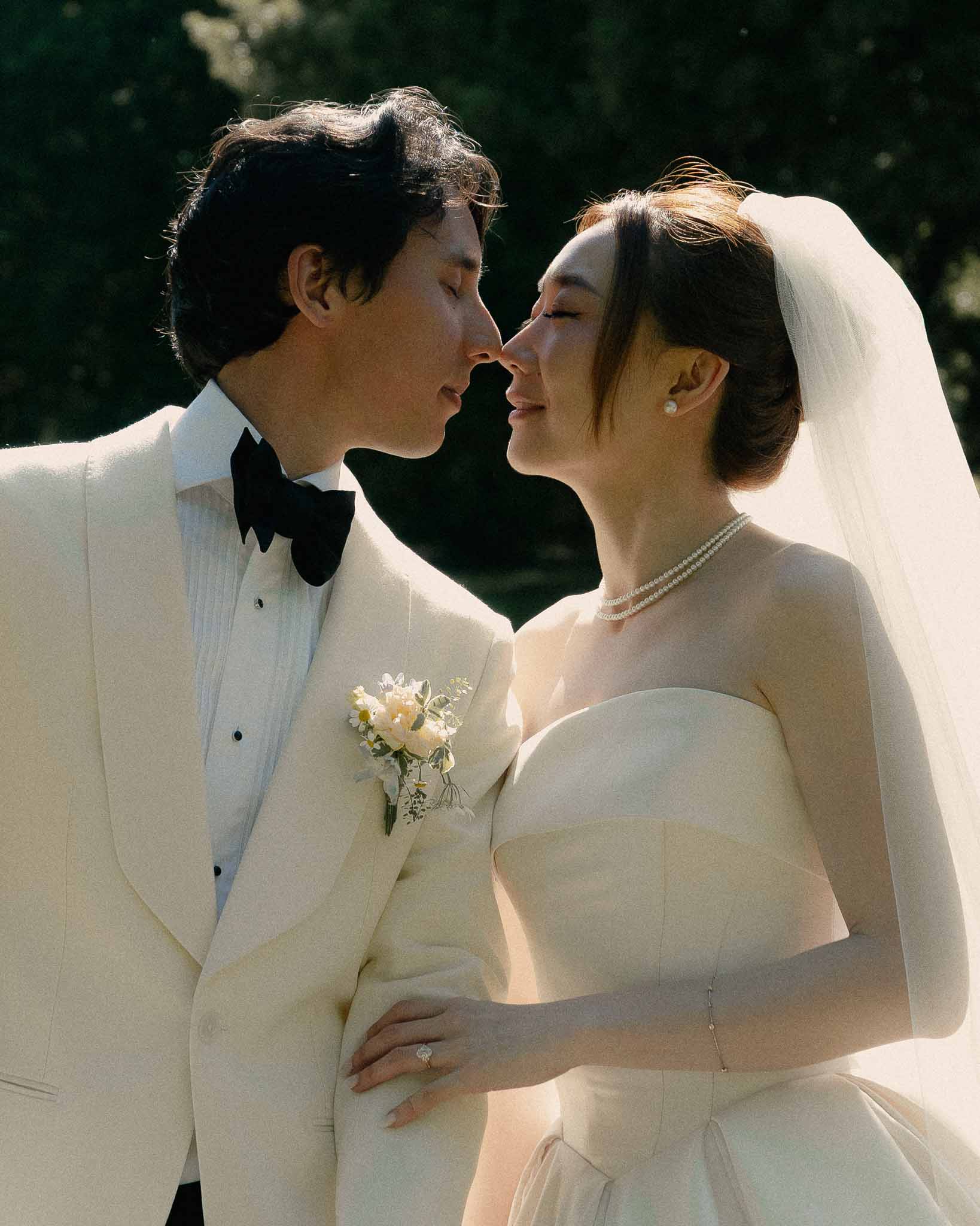Close-up of bride and groom with eyes closed in intimate moment, pearl choker and cream boutonniere at golden hour