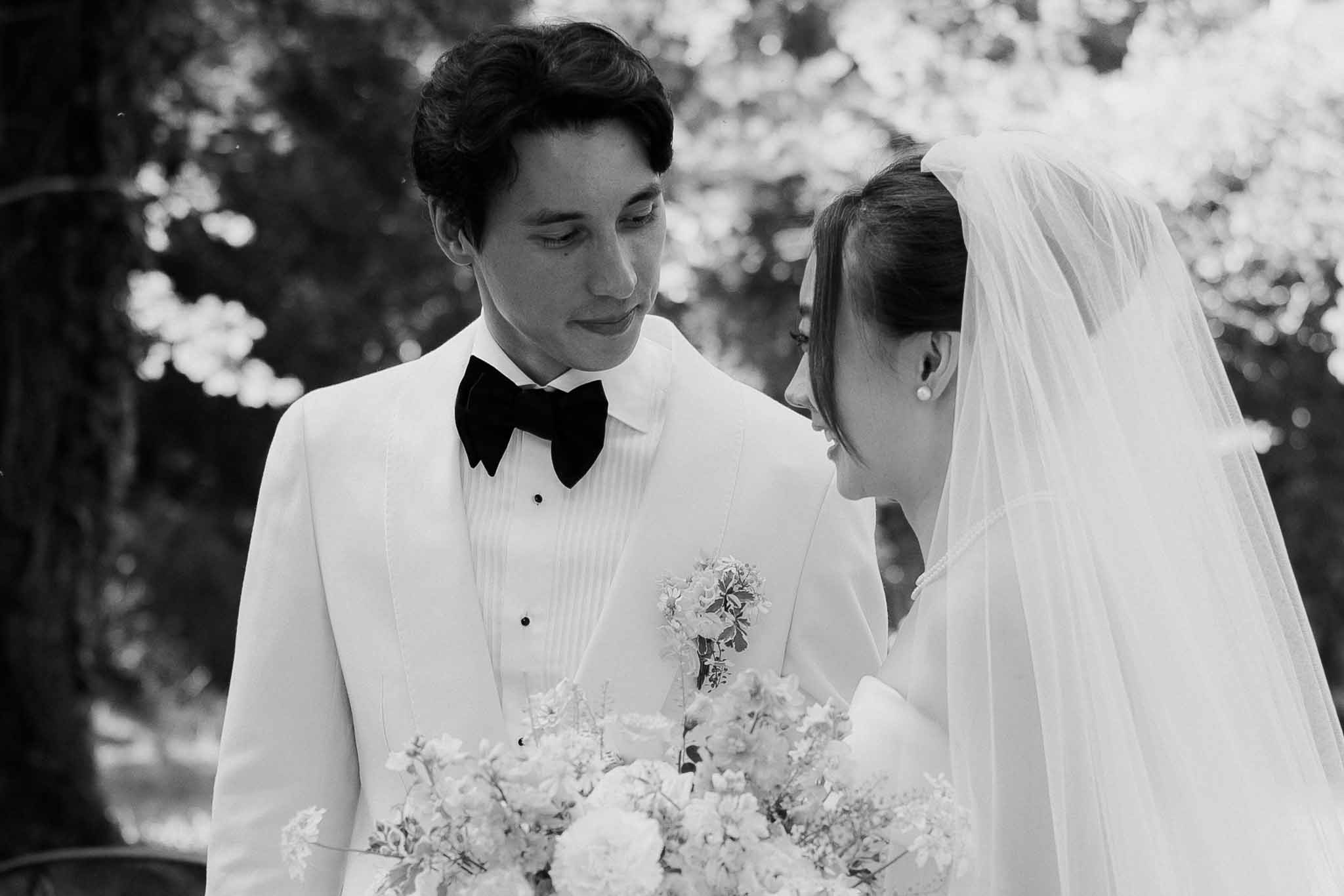 Black and white close-up couple facing each other bride with veil and peony bouquet groom in white dinner jacket