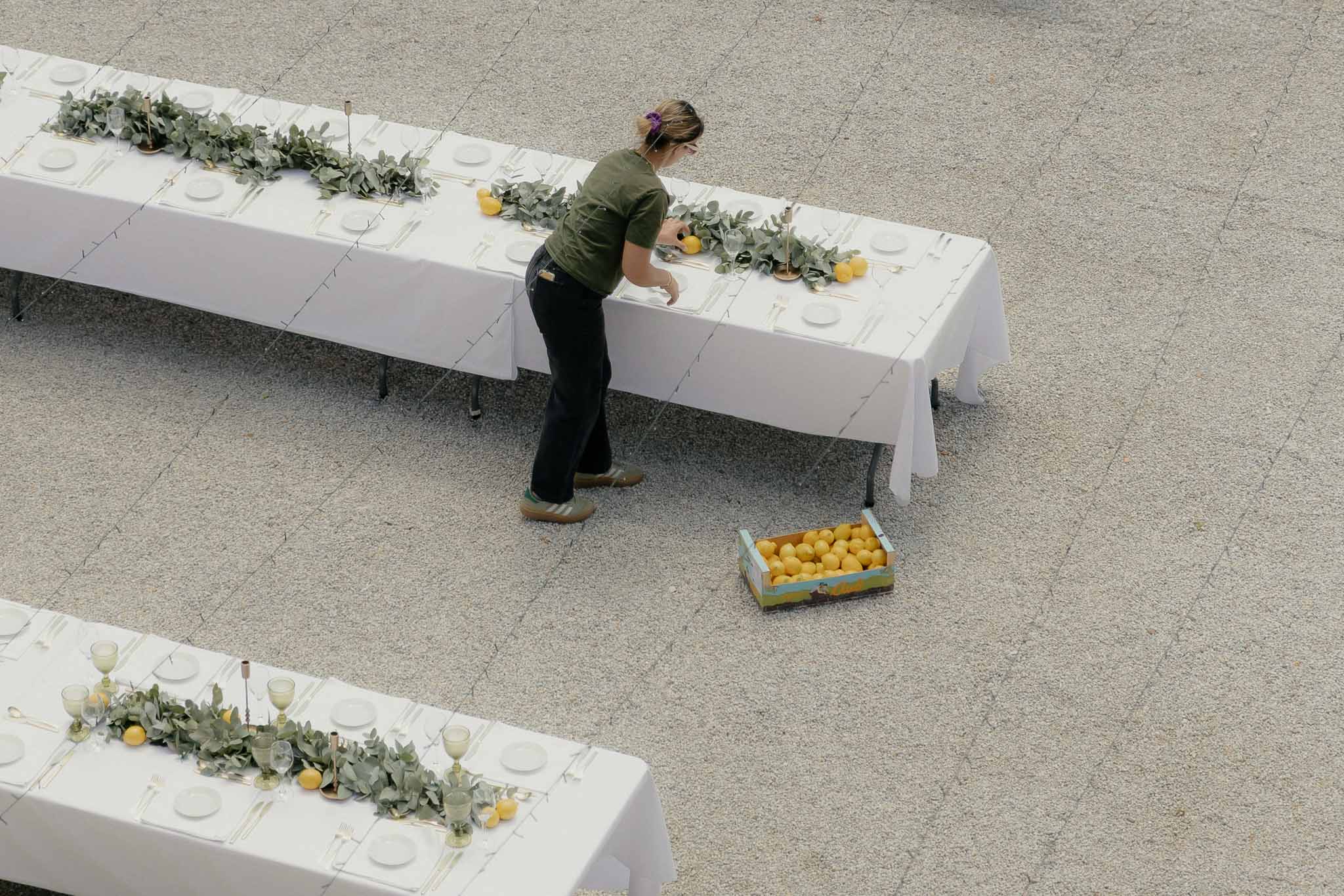 Aerial view of eucalyptus garland with whole lemons on white linen table with green-tinted glasses