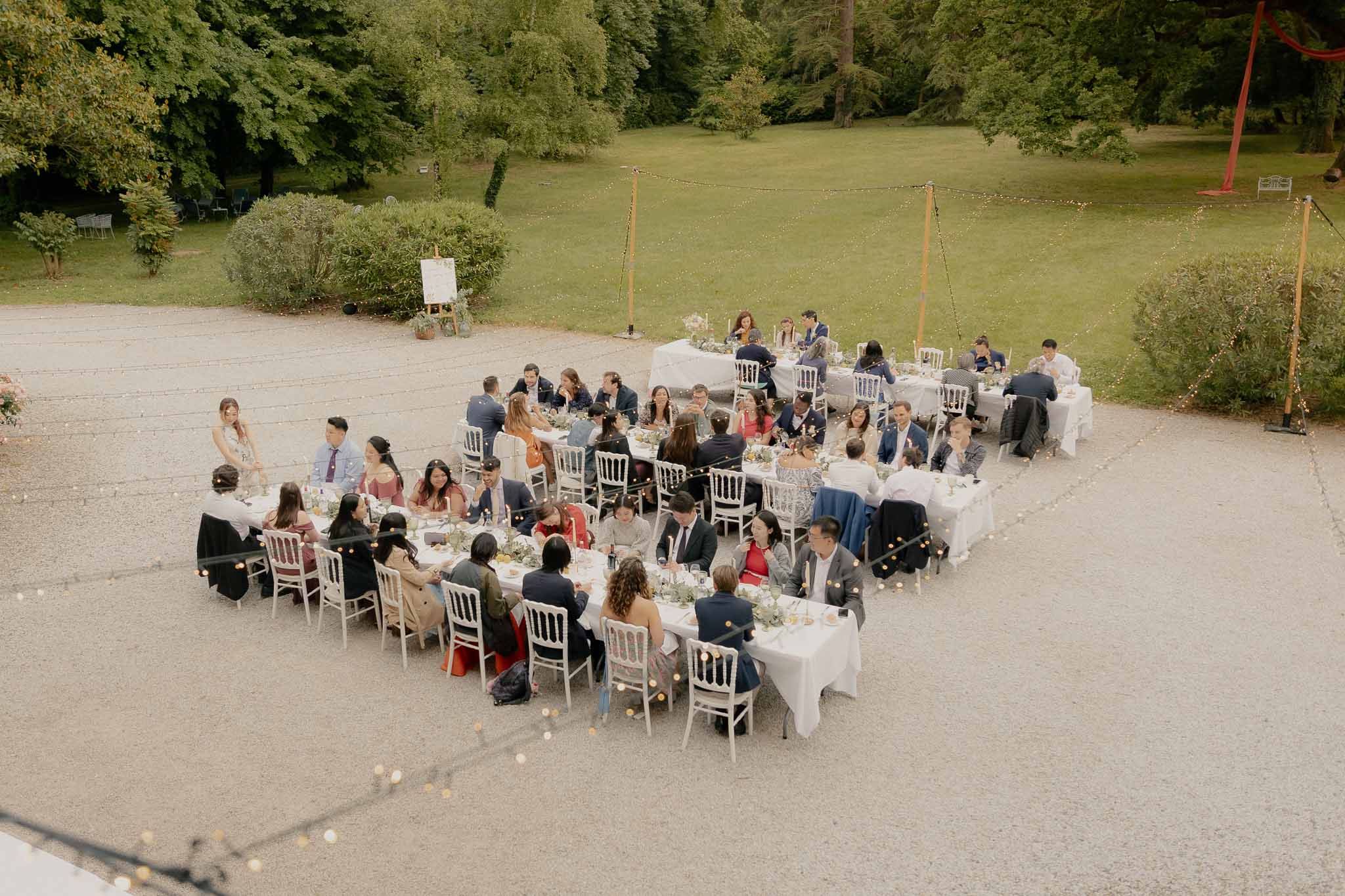 Aerial view of outdoor reception dinner with 50 guests at U-shaped tables lit by fairy lights