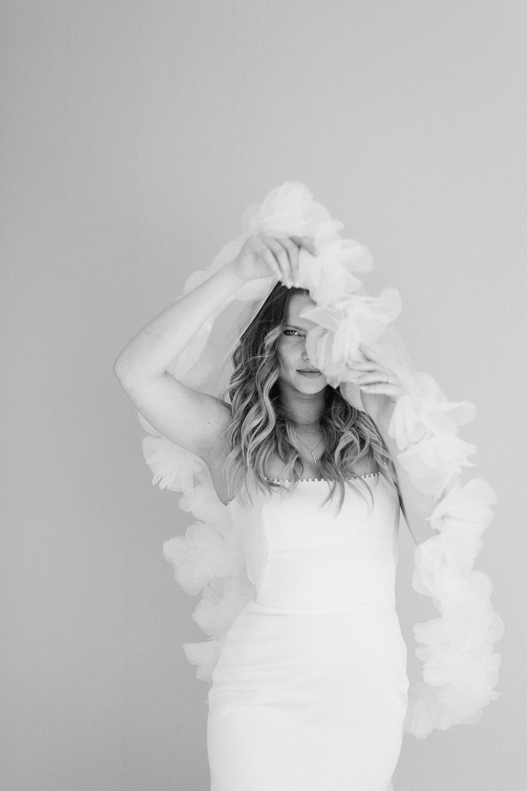 Black and white bride in strapless gown holding floral-trimmed veil over face in editorial studio portrait