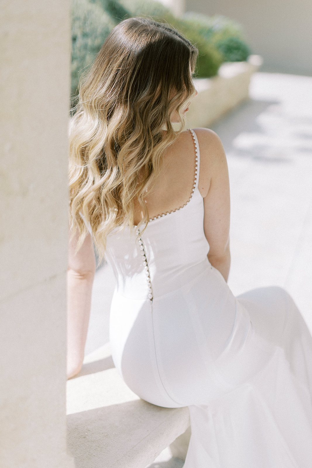 Rear portrait of bride in fitted spaghetti-strap gown with pearl button closures on stone terrace