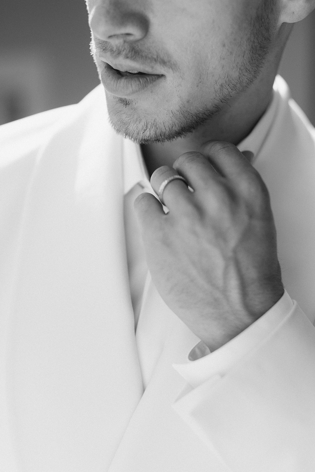 Black and white close-up of groom adjusting shirt collar with wedding band visible on right hand