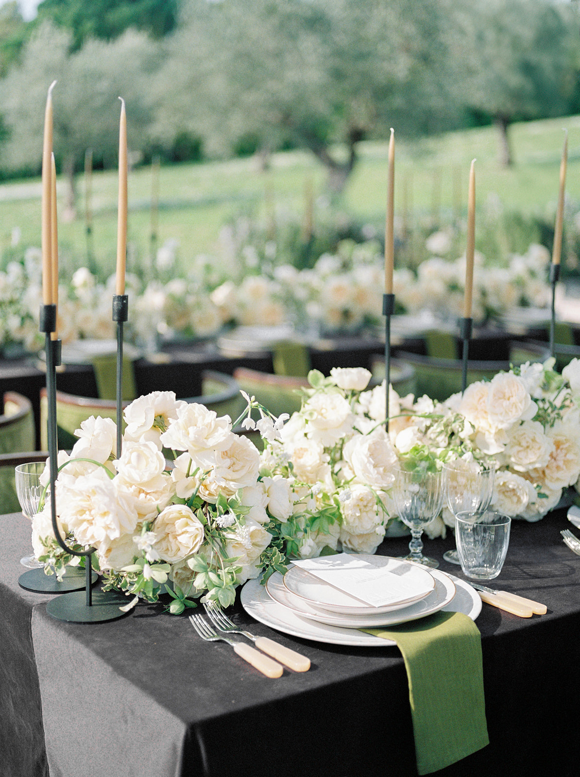 Charcoal linen table with cream rose runner, black iron candleholders, and gold-rimmed place settings