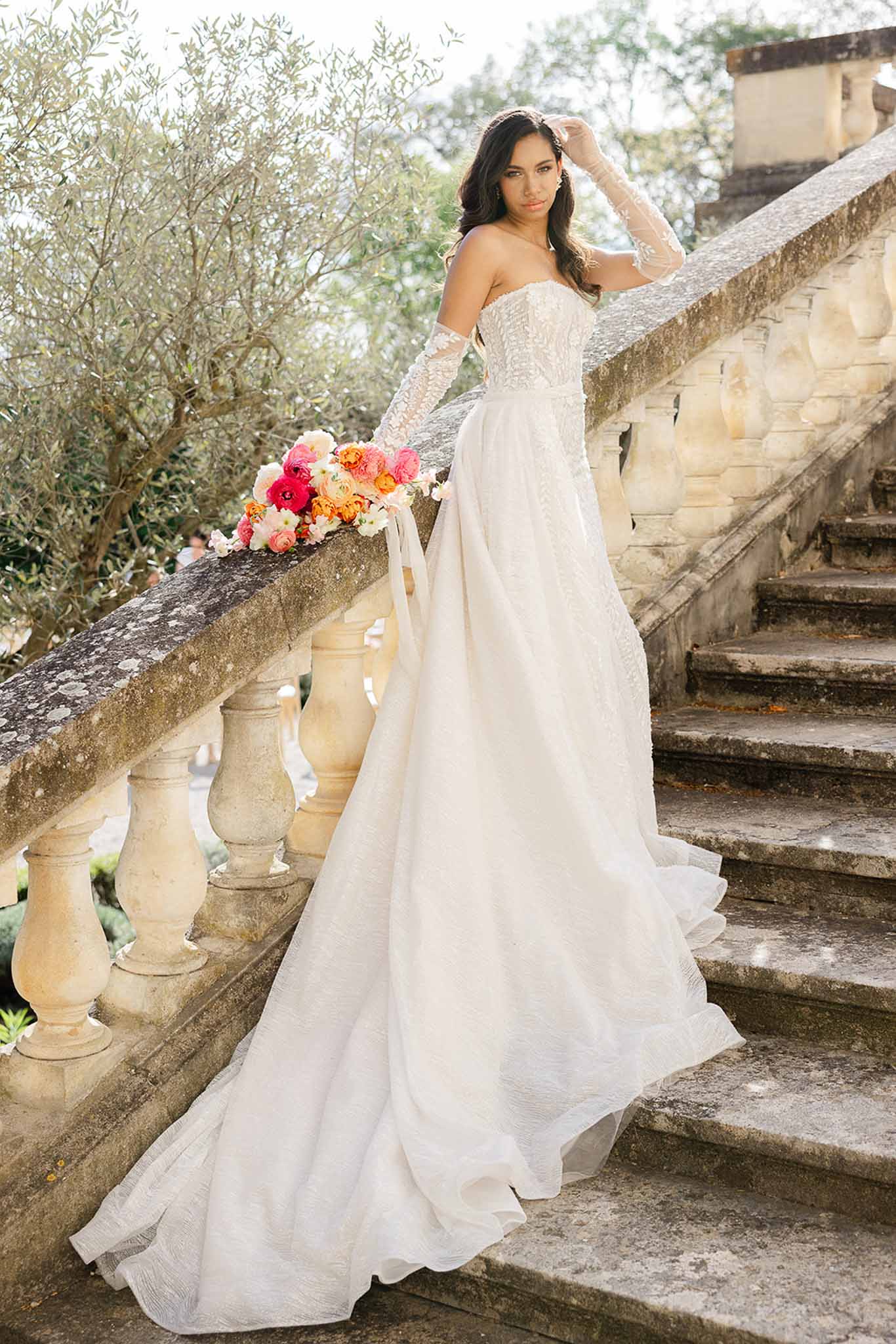 Bride with pink blush bouquet in lace gown and gloves on stone stairs at Château Martinay