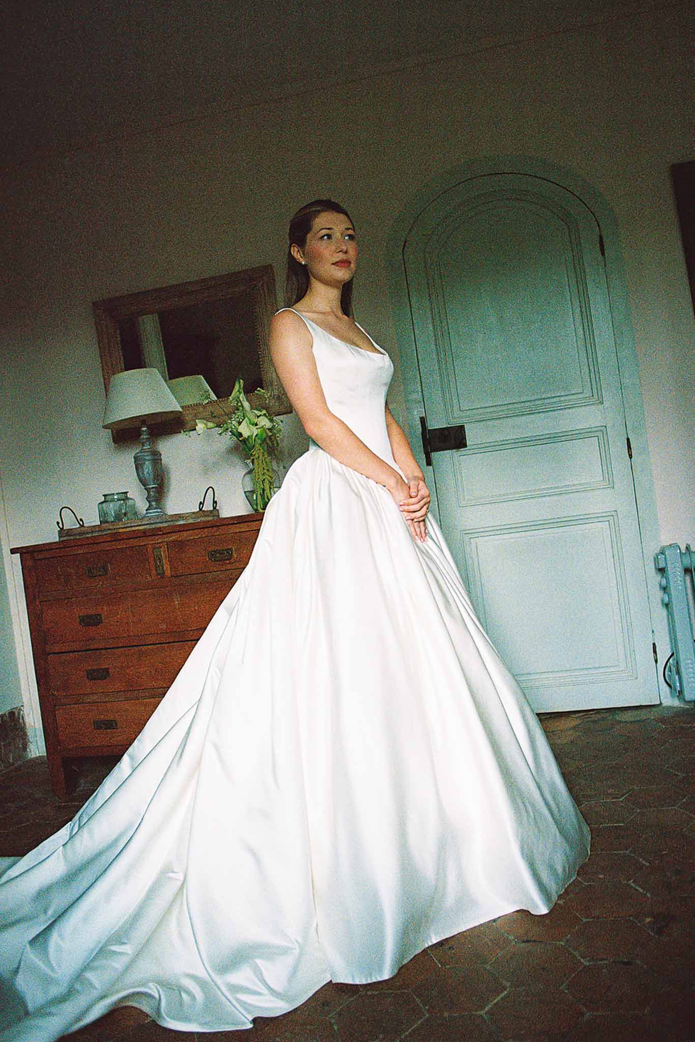 Bride in white satin square-neck ballgown with long train in French provincial room with blue arched door