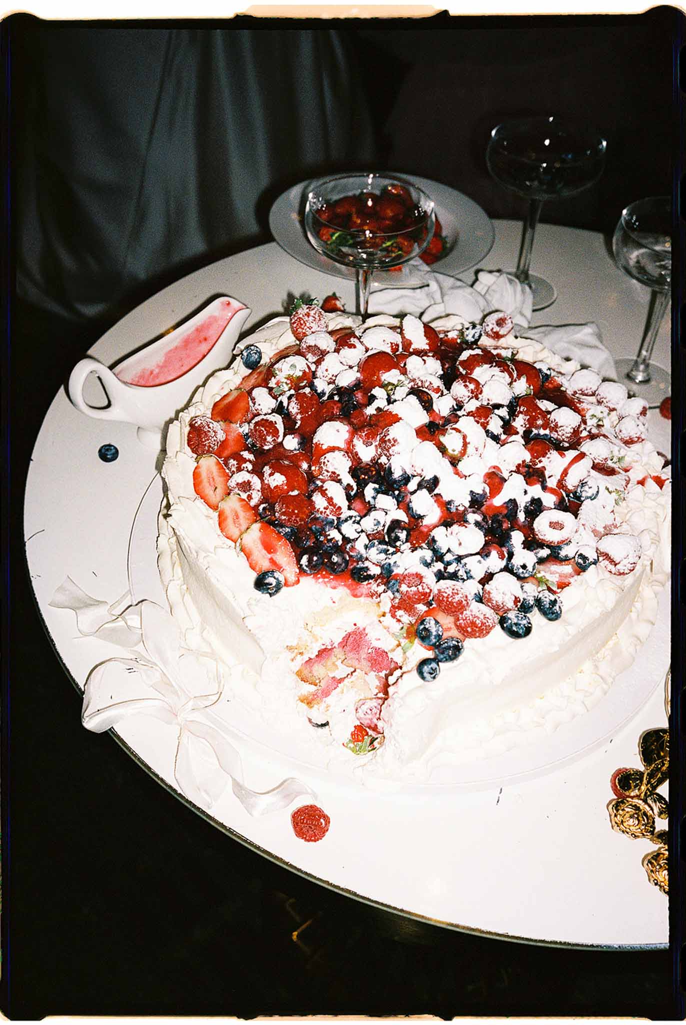 Pavlova-style wedding cake topped with fresh strawberries blueberries and raspberries with berry coulis at indoor reception