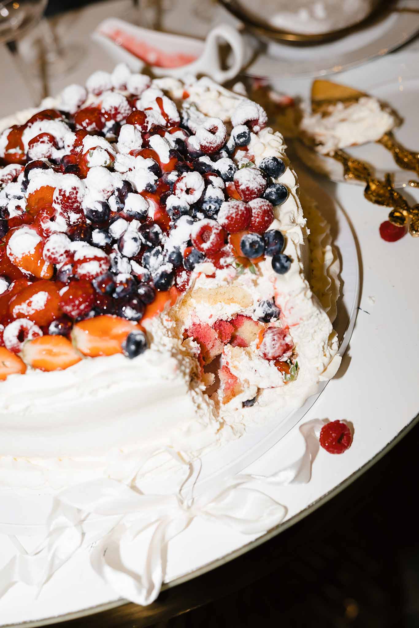 Berry-topped cream cake with strawberries, blueberries, and raspberries on gold-rimmed platter, slice removed