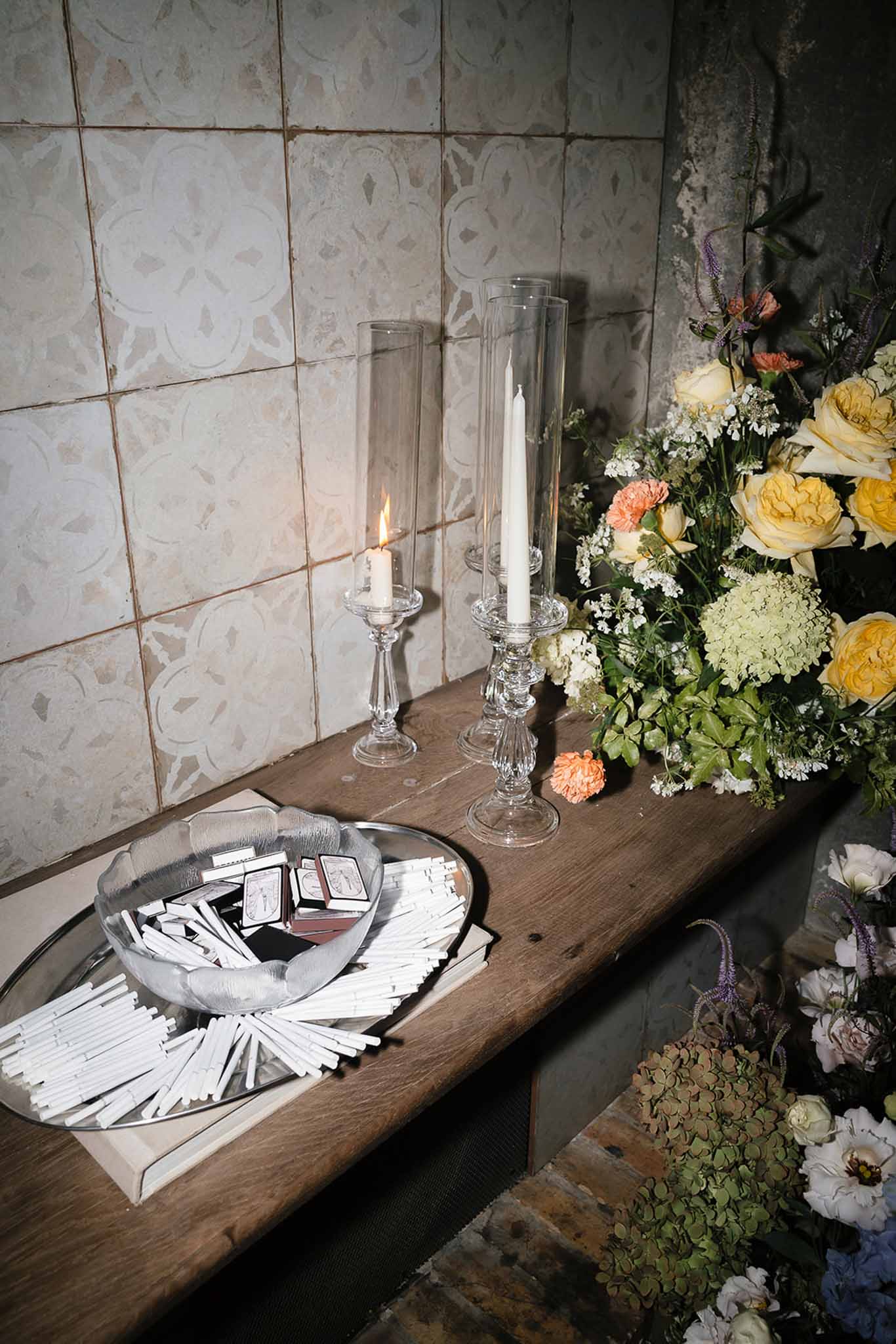 Cocktail station with yellow roses, peach carnations, lavender spikes, hurricane candles, and matchboxes