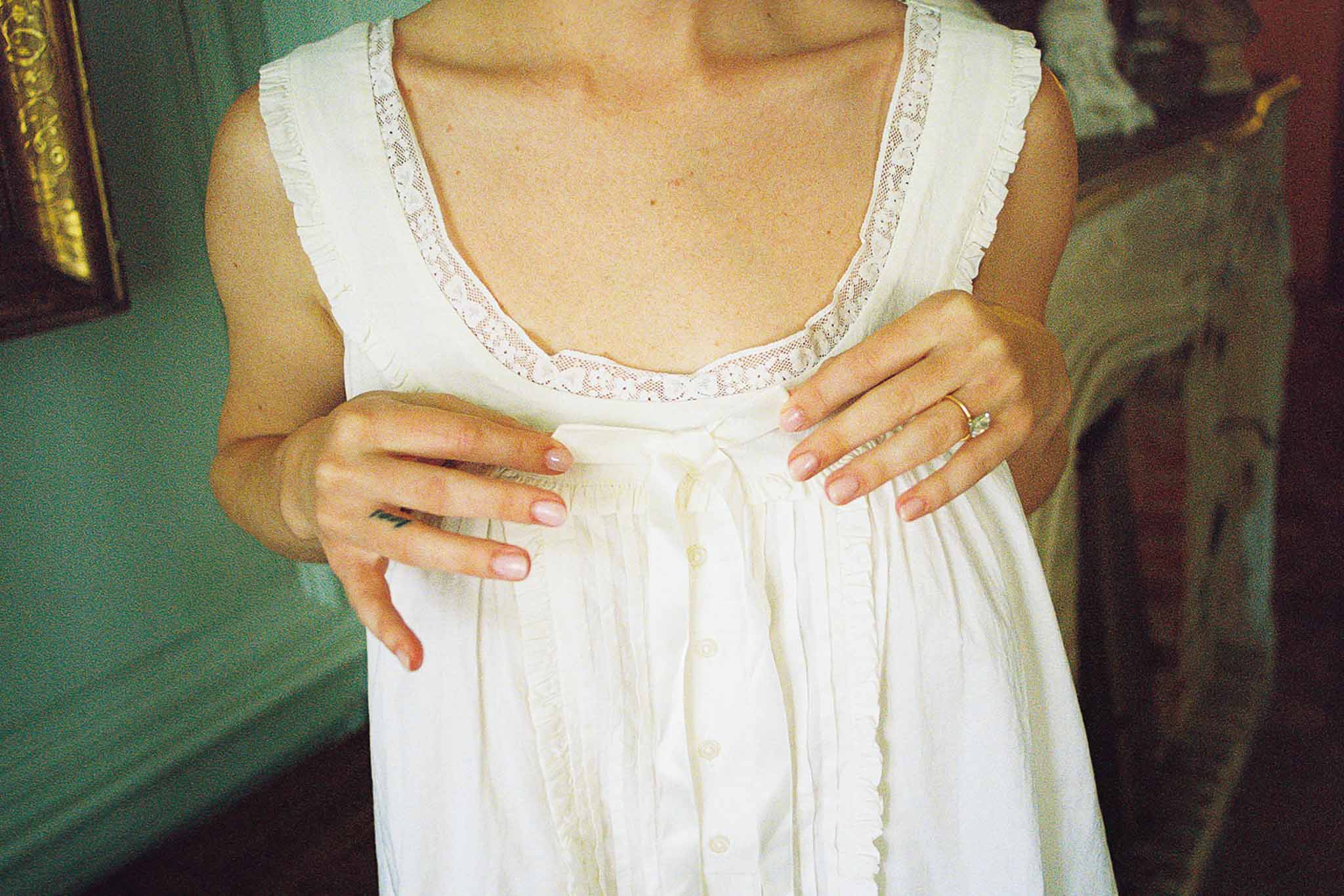 Close-up of bride adjusting ribbon on white cotton slip with lace trim in chateau room