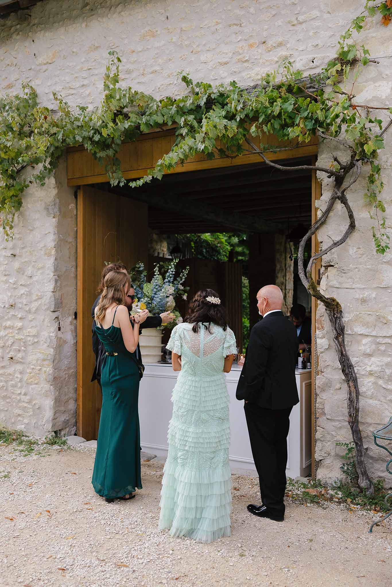 Four guests gathered at stone bar window draped in climbing vine with blue delphinium arrangement