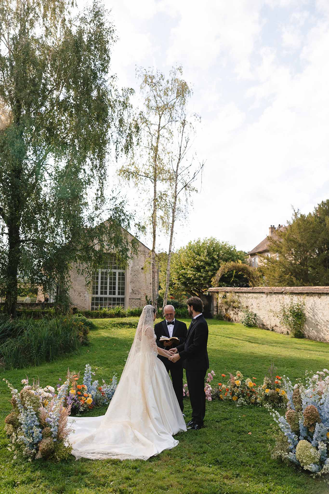 Ceremony with boho pastel aisle flowers of delphiniums, marigolds, and pampas before stone barn