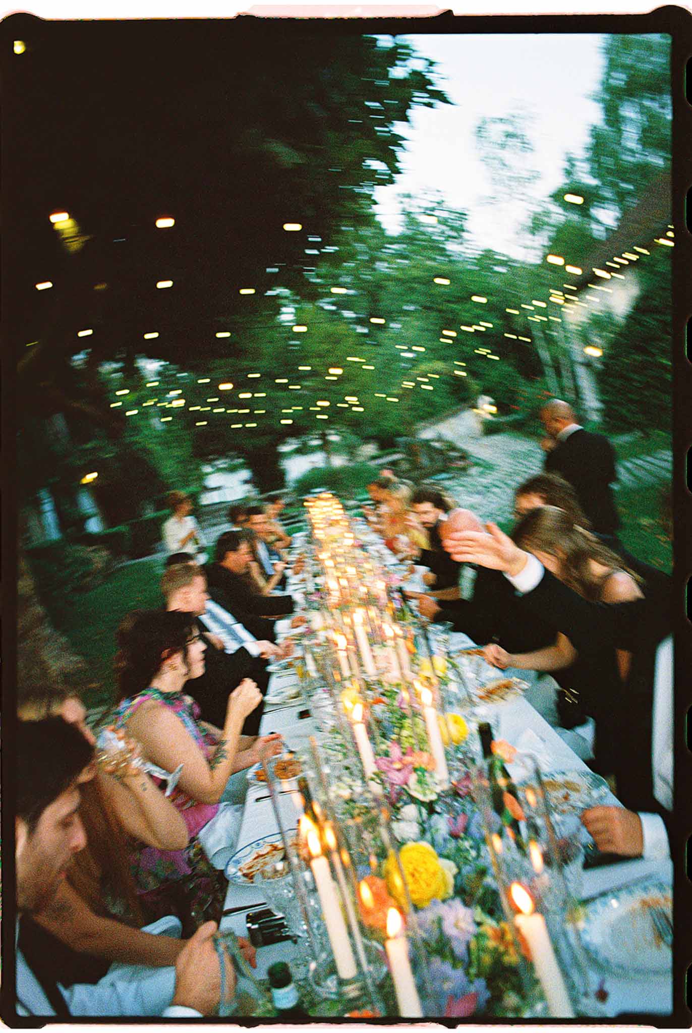 Film photograph of evening reception table with colorful floral runner and Edison lights at dusk