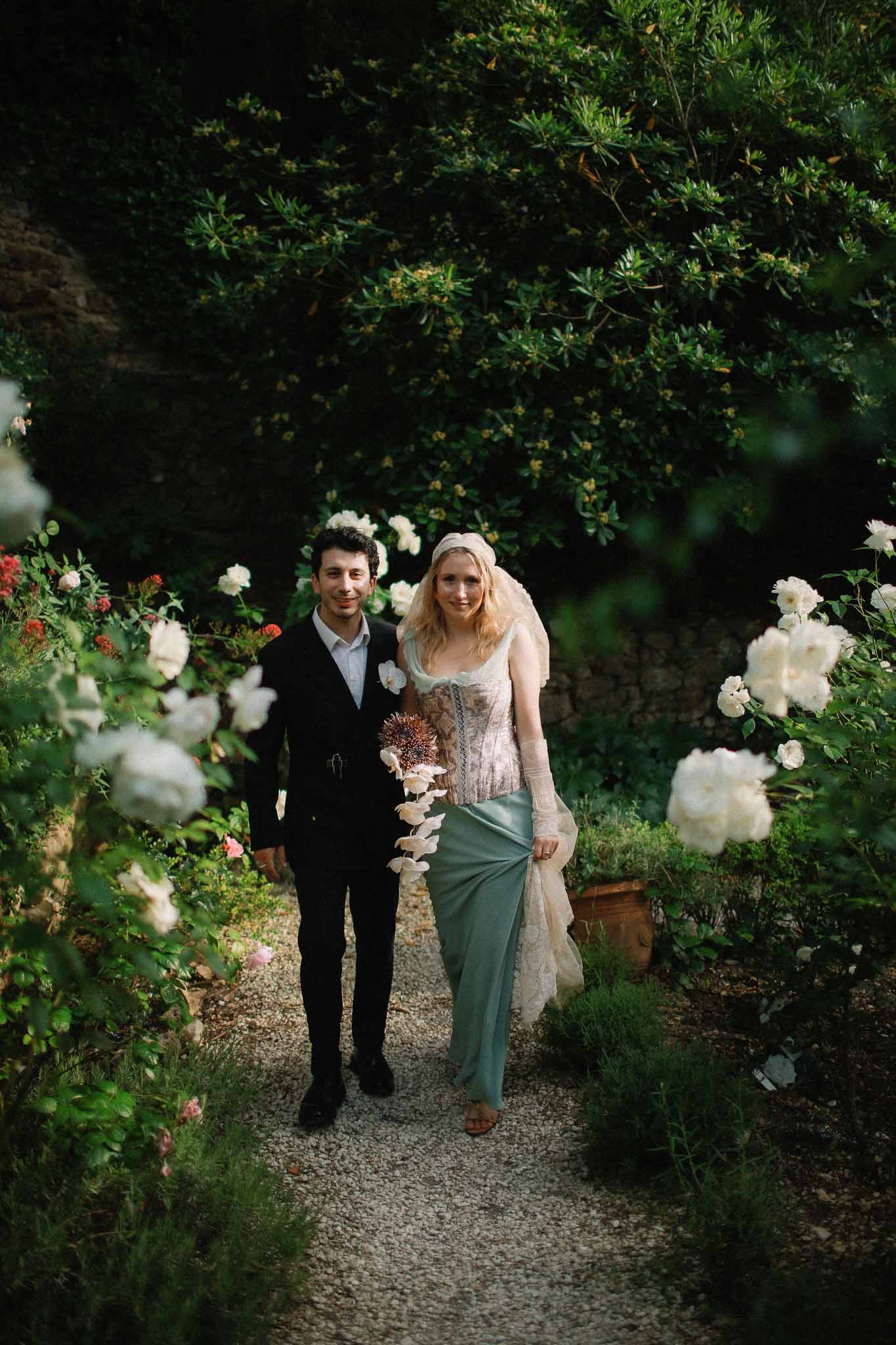 Bride and groom walking through flowering garden at Chateau St Victor Lacoste