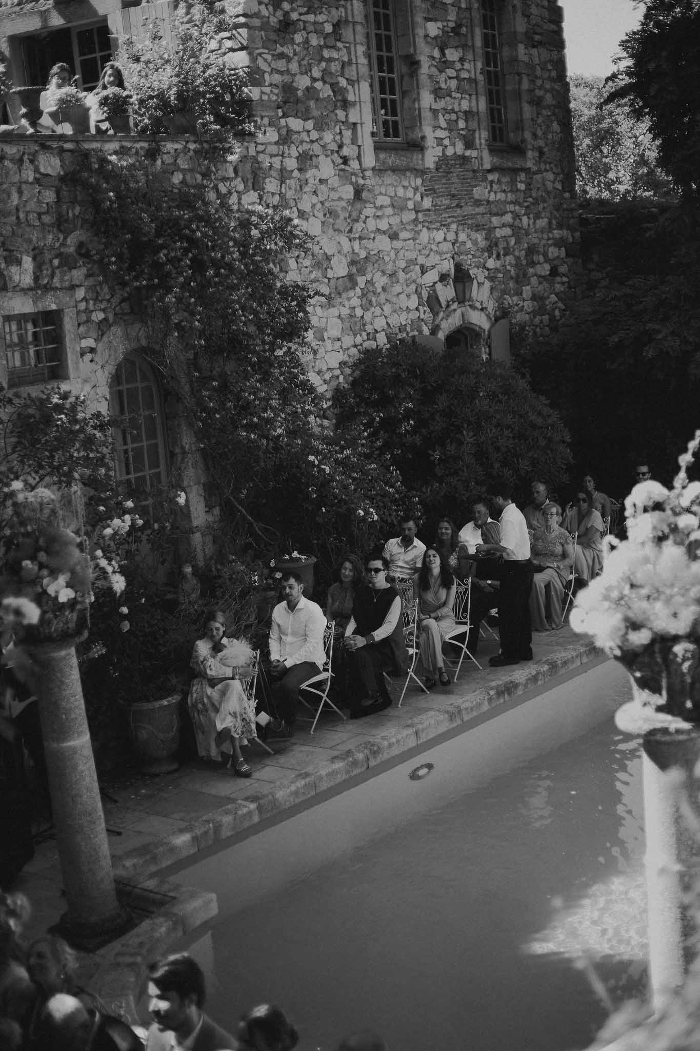 Wedding guests seated beside the pool during ceremony at Chateau St Victor Lacoste