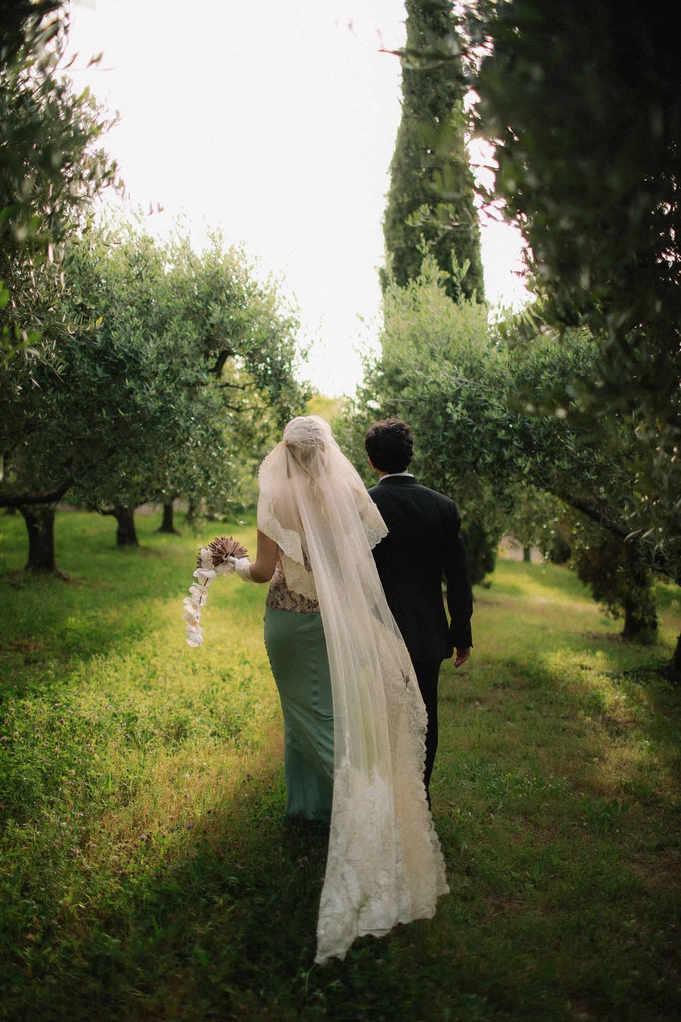 Long lace veil trailing as bride and groom walk at Chateau St Victor Lacoste