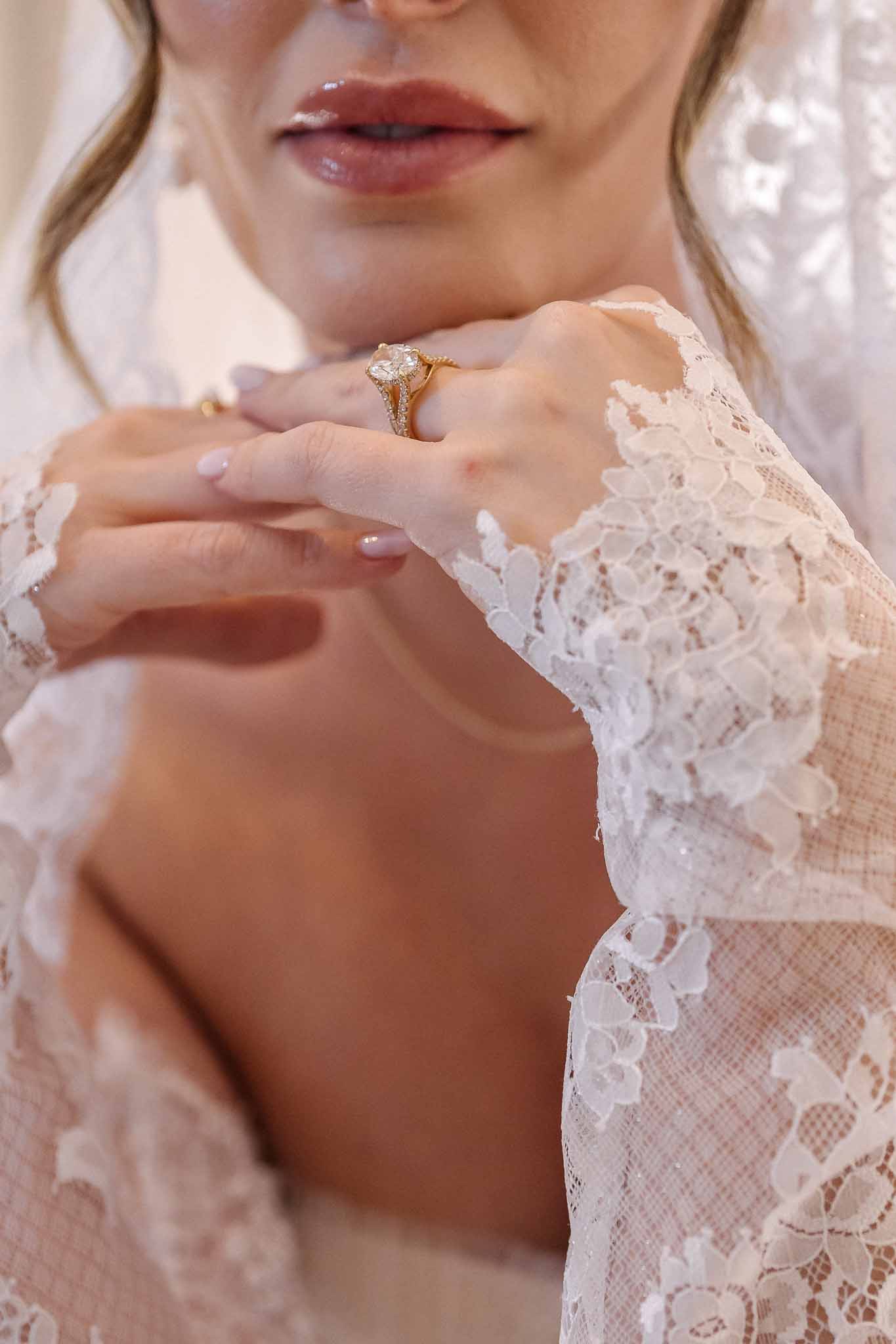 Close-up of bride's hands in lace sleeves with oval diamond engagement ring and gold wedding band