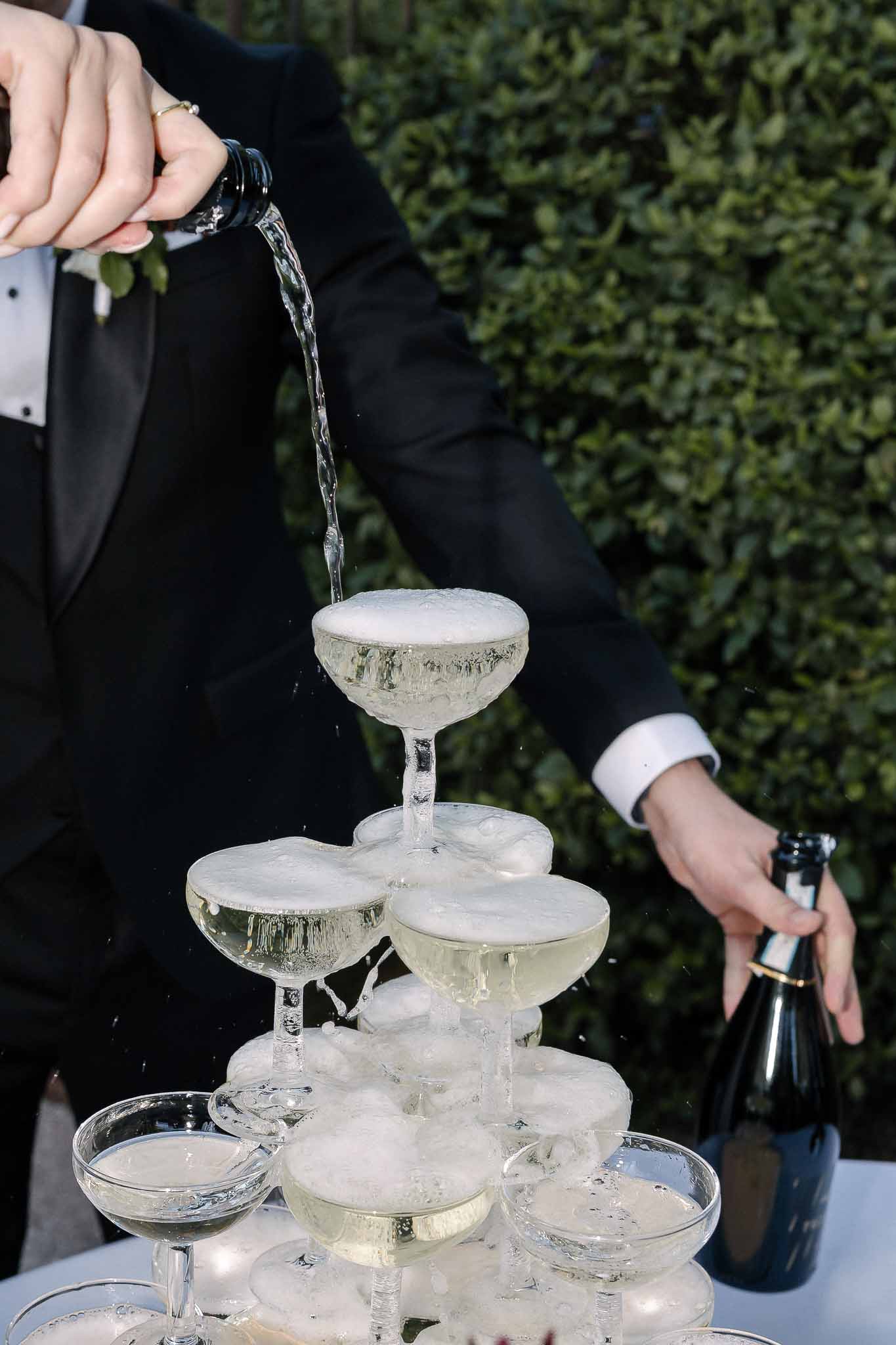Champagne being poured into coupe tower cascading through multiple tiers at outdoor reception