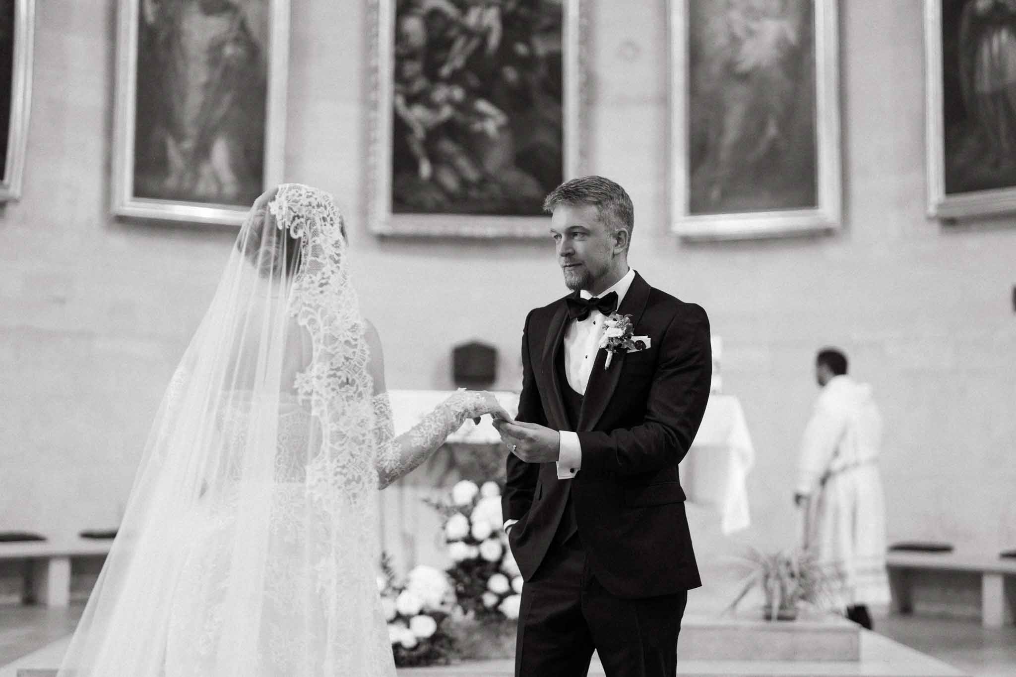 Black and white ring exchange in formal church with mantilla veil and floral altar arrangements