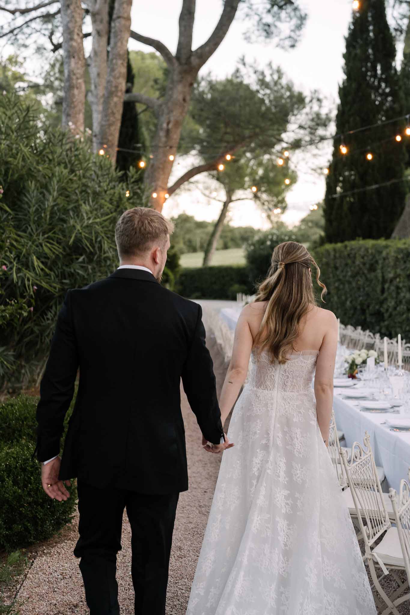 Couple walking hand in hand past blue linen reception table with taper candles and festoon lights