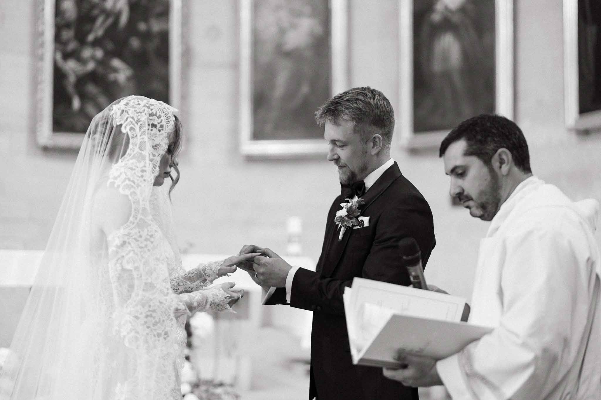 Black and white ring exchange in chapel with mantilla lace veil and officiant reading from book