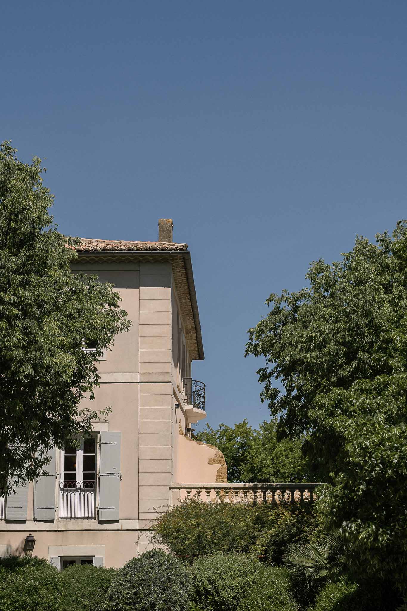 Beige-pink bastide with terracotta roof, Juliet balconies, grey-blue shutters, and stone balustrade terrace