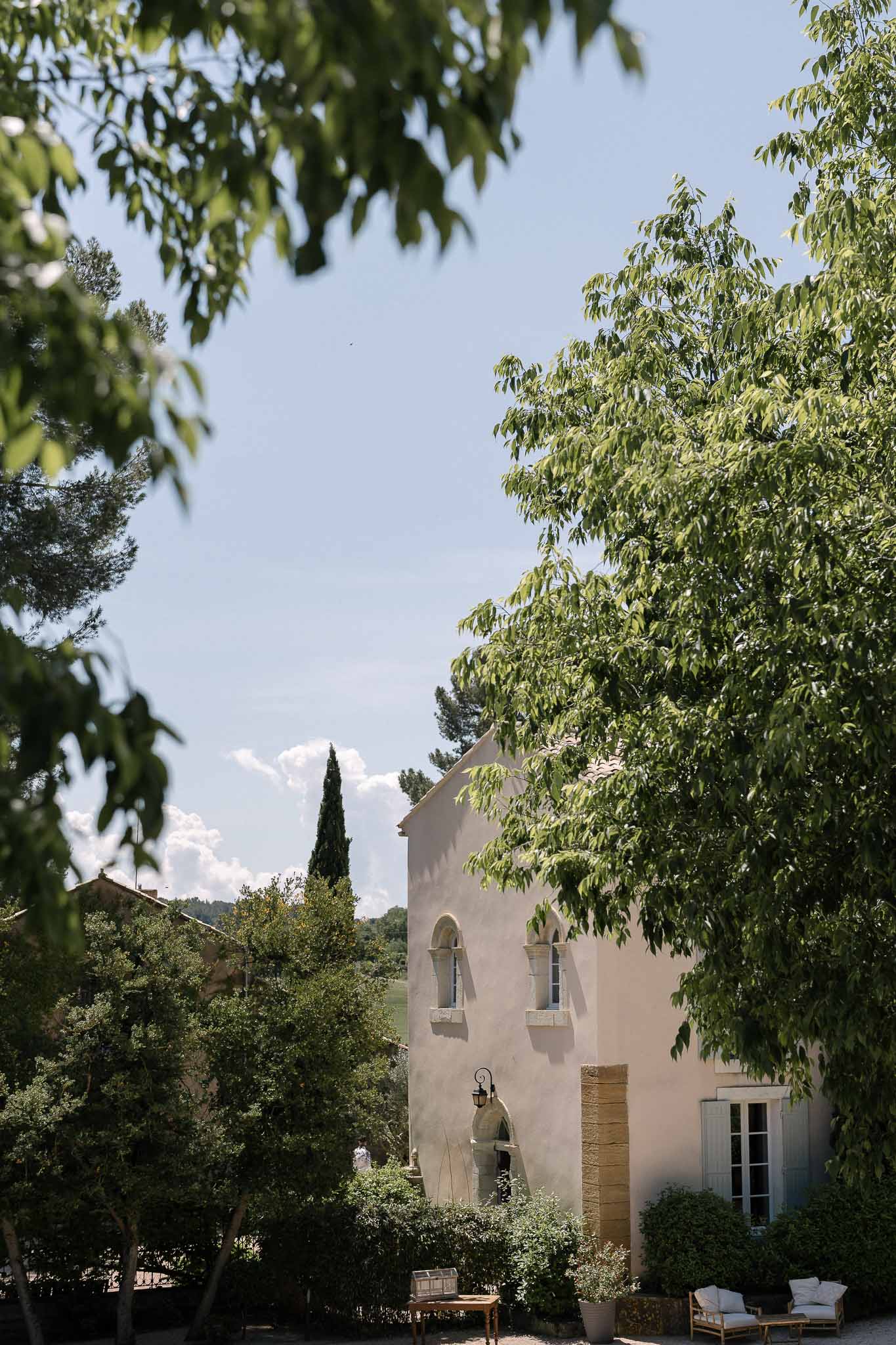 Ochre Provencal bastide with arched windows, cypress tree, and wicker seating on courtyard terrace
