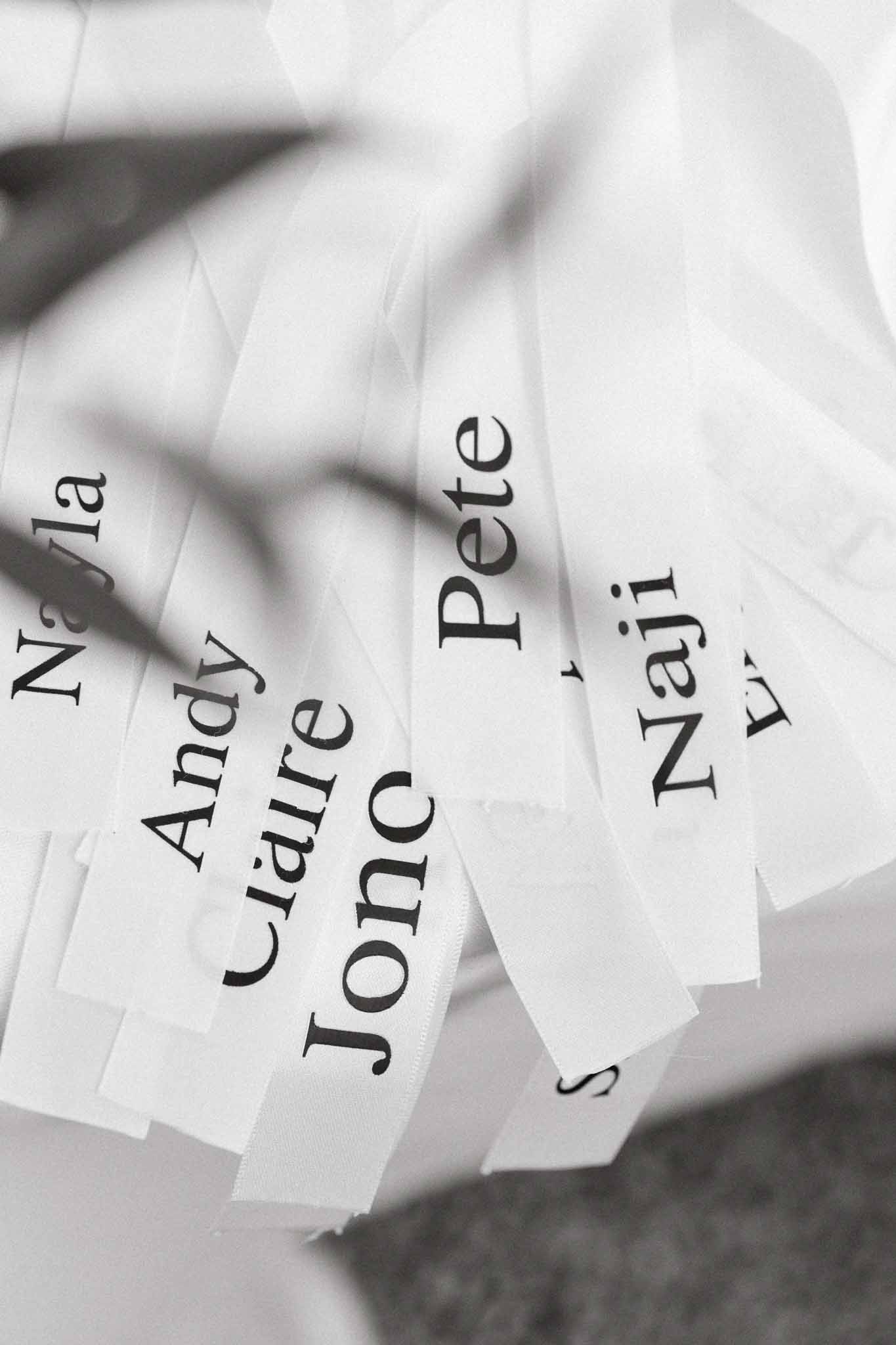 Black-and-white close-up of white ribbon place cards printed with guest names in serif font