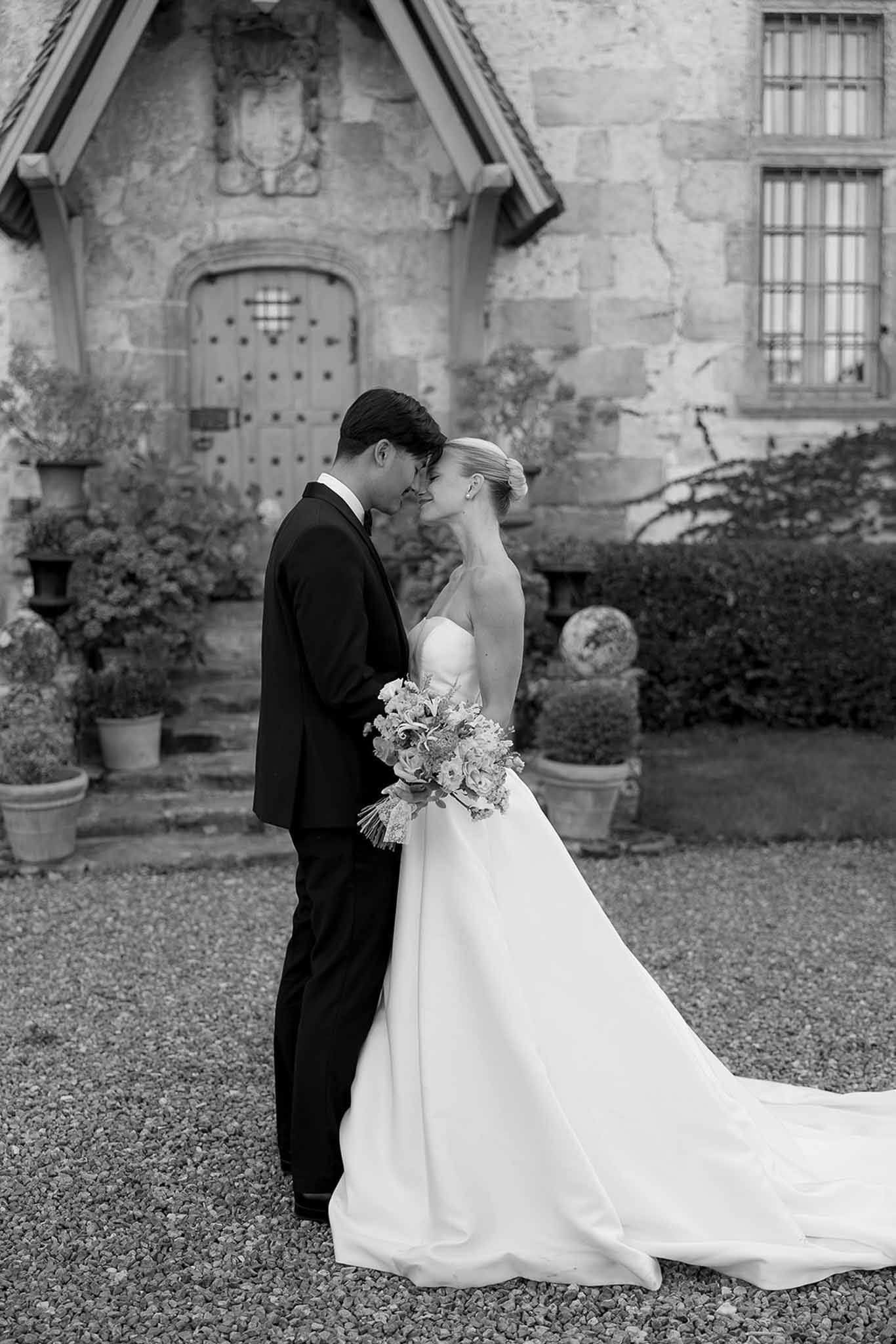 Black and white portrait of couple touching foreheads before carved stone chateau entrance