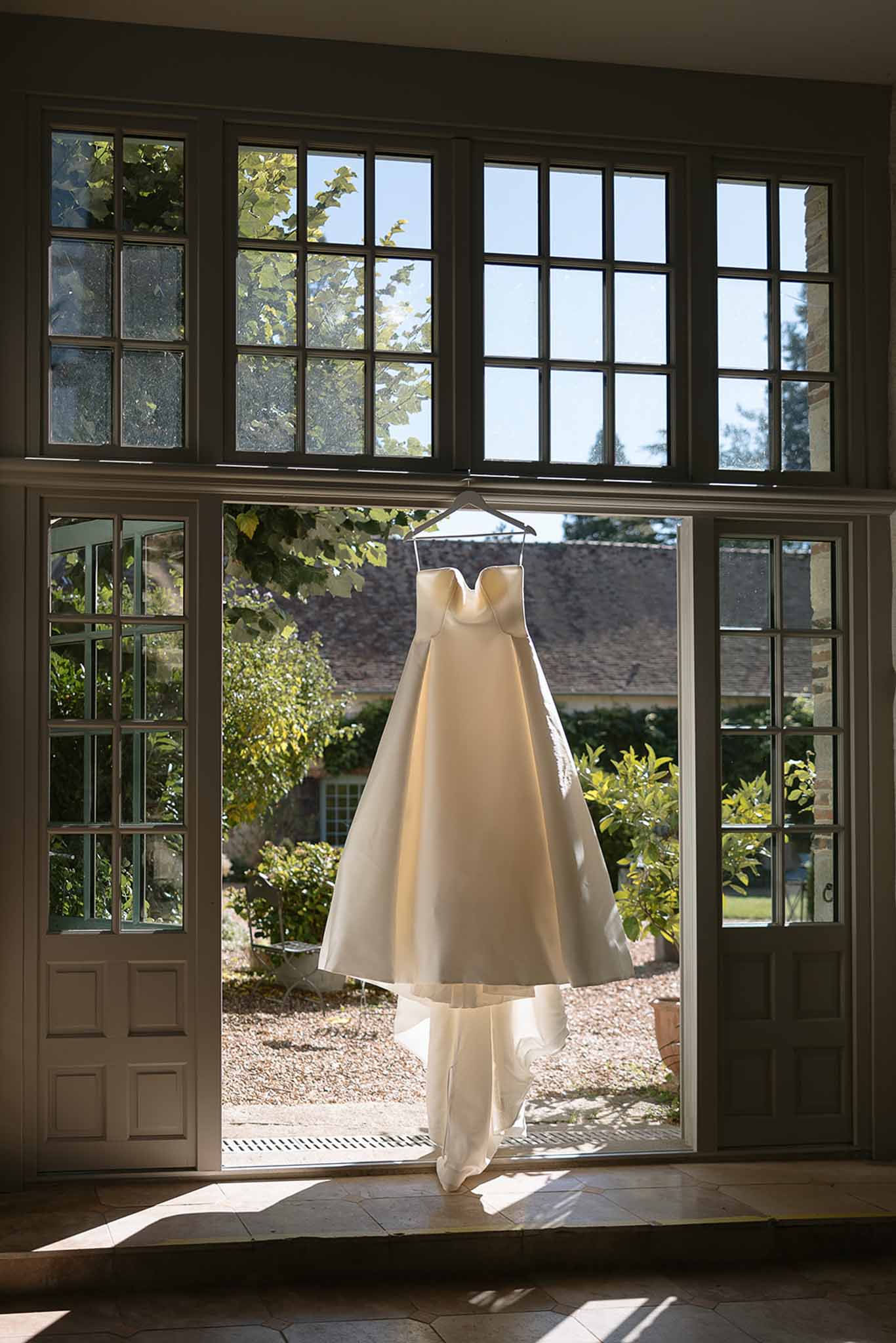 Ivory strapless ballgown hanging in open French doors with chateau courtyard visible beyond